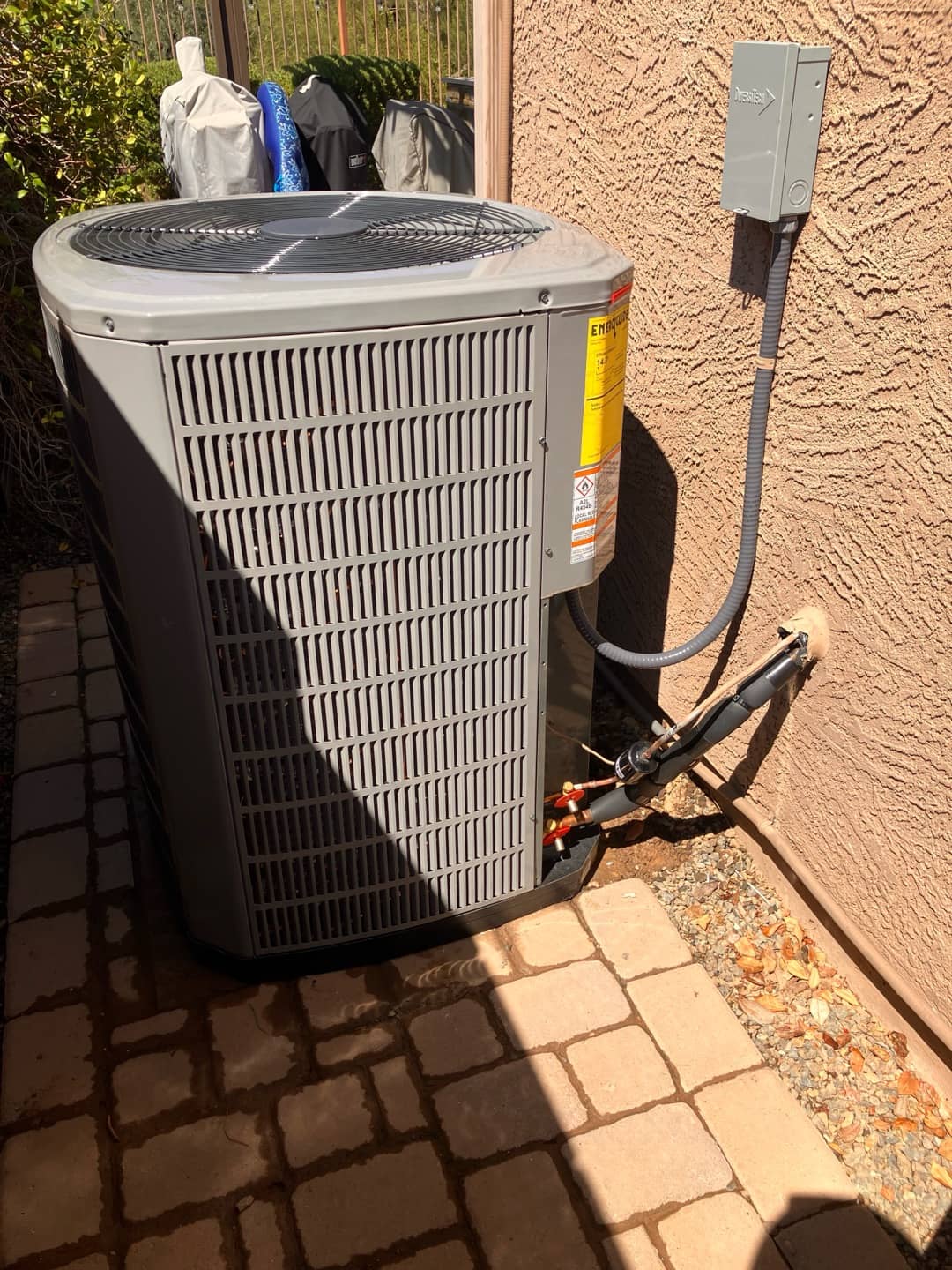 New outdoor condenser set on a level pad with insulated refrigerant lines and weatherproof disconnect mounted on the wall.