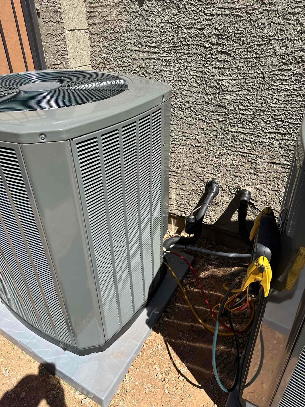 New outdoor condenser set on a level pad with insulated refrigerant lines routed to the wall penetrations.