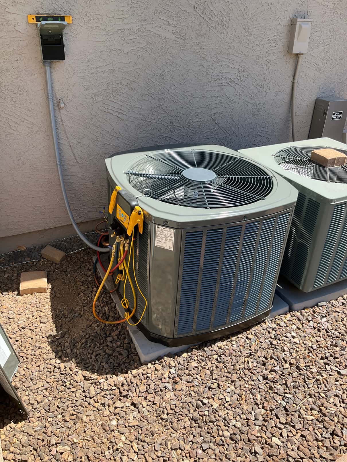 New outdoor condenser set on a level pad with refrigerant hoses connected and electrical whip and disconnect mounted on the wall.