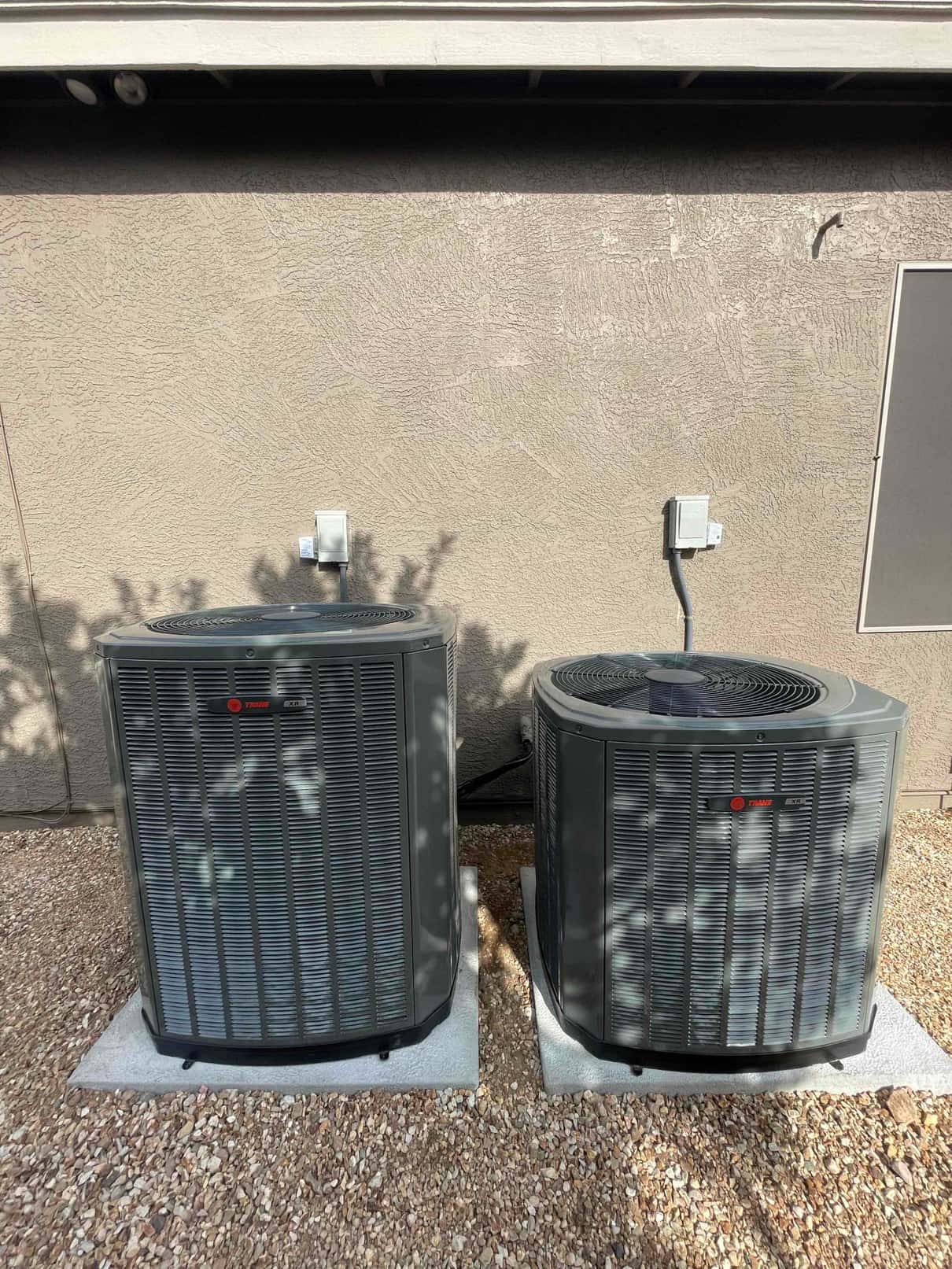 Two new outdoor condensers set on level pads with electrical disconnects mounted on the wall behind.
