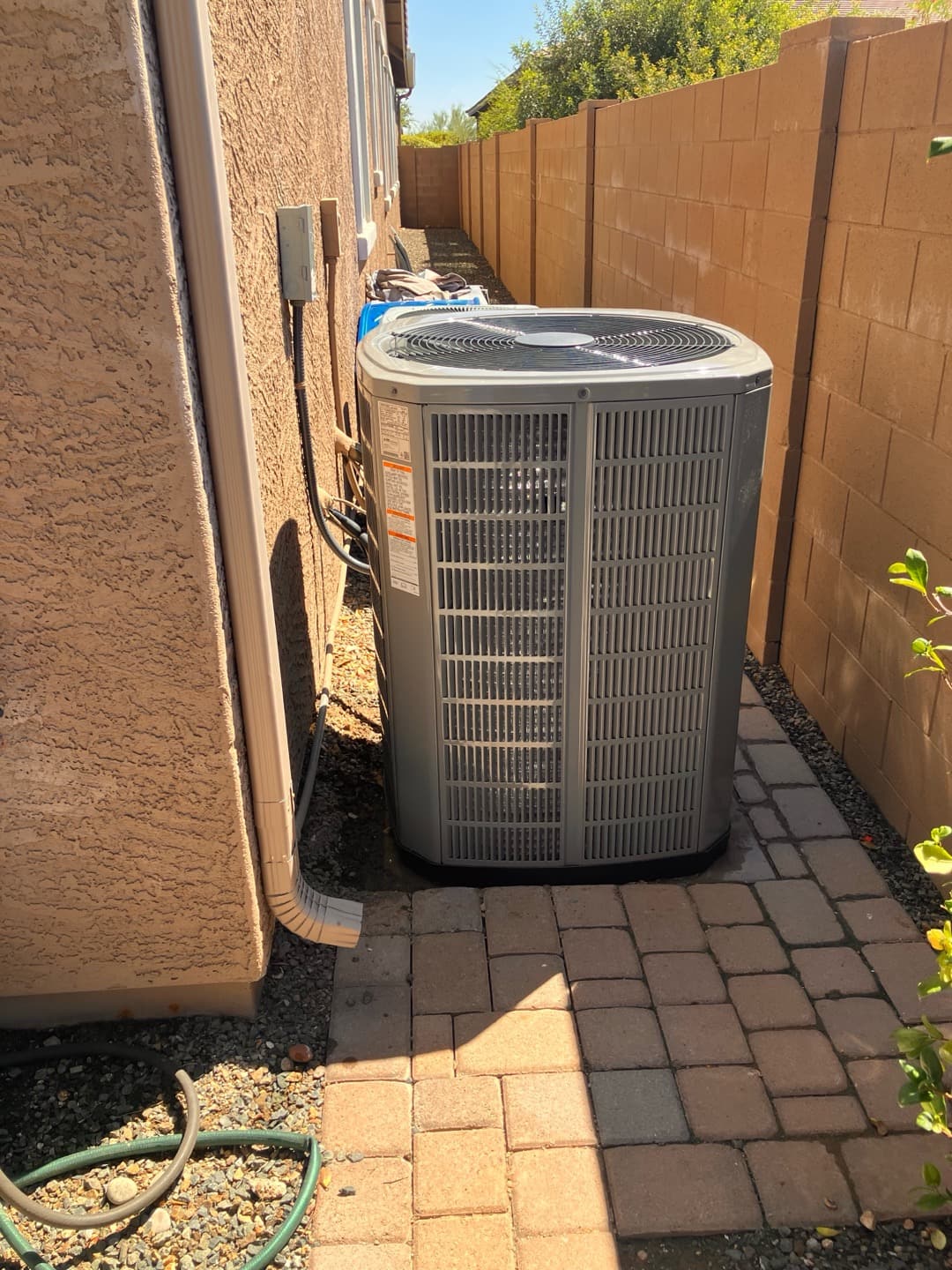 New outdoor condensing unit installed on a level paver pad with line set cover and electrical disconnect mounted on the wall.