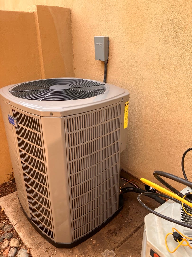 New outdoor heat pump condenser set on a level pad with disconnect mounted on the wall and insulated line set connected.