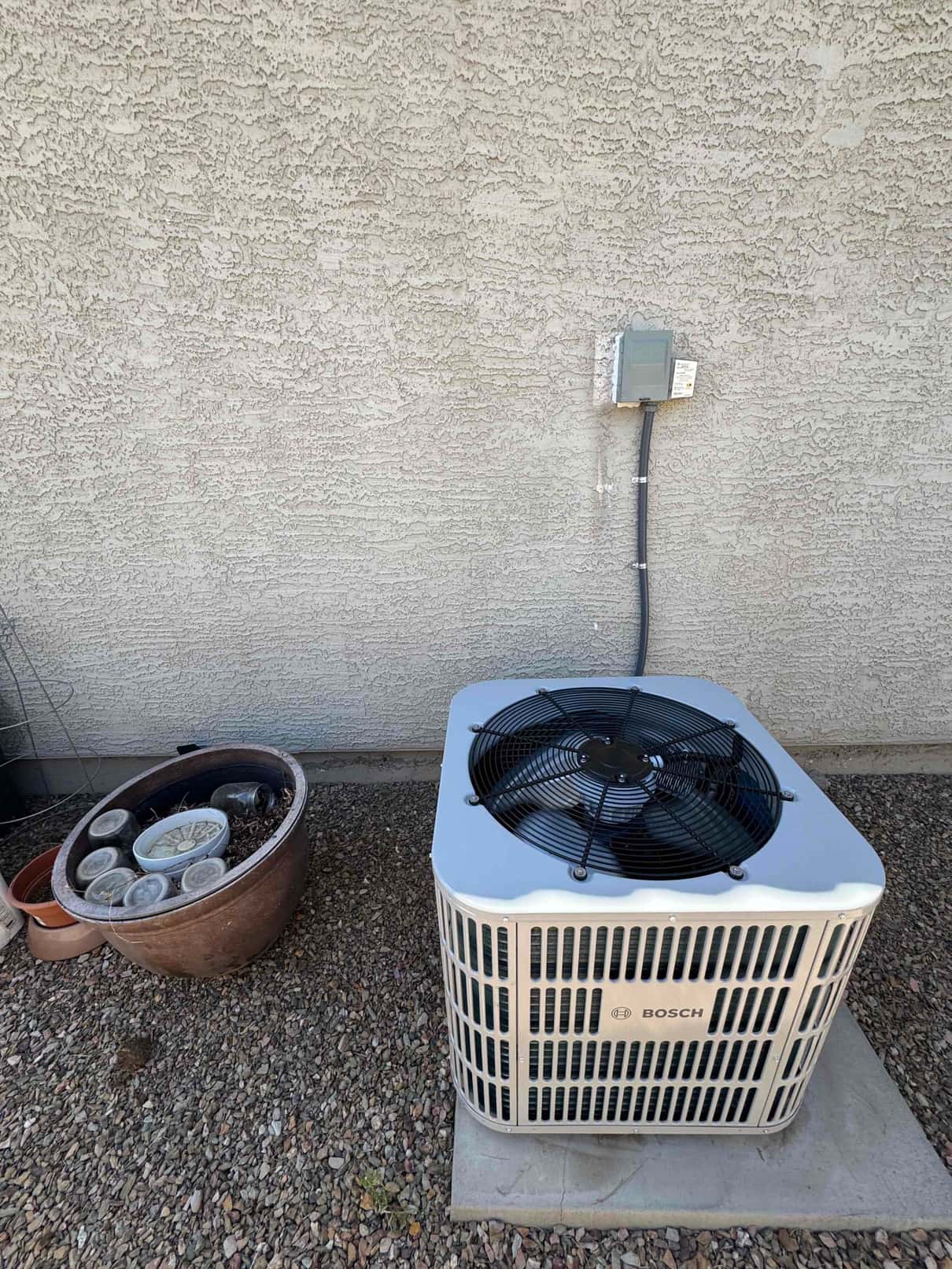 New outdoor heat pump condenser set on a level pad with electrical disconnect mounted and conduit secured to the exterior wall.