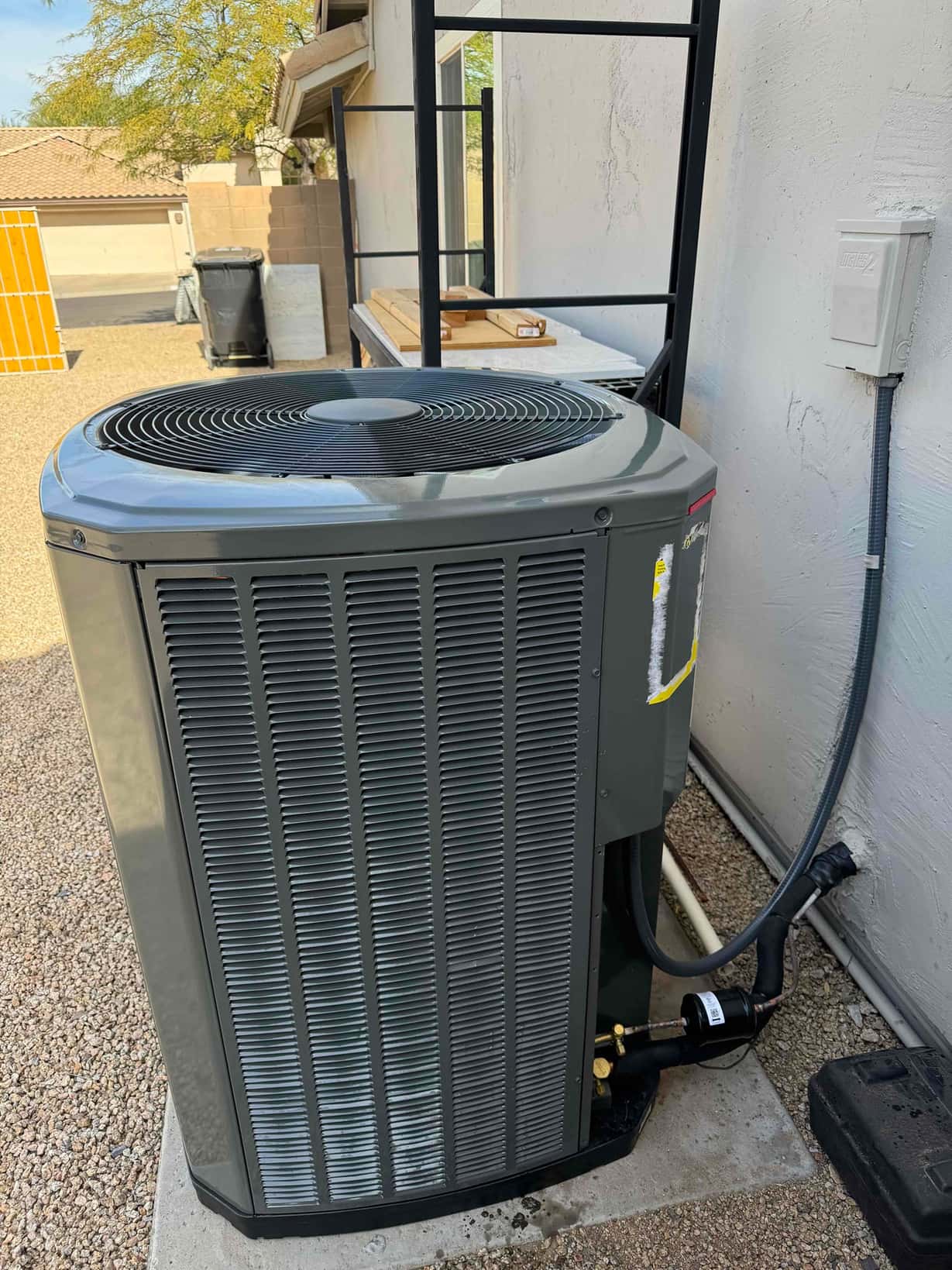 New outdoor heat pump condenser set on a level pad with insulated line set and weatherproof electrical whip connected.
