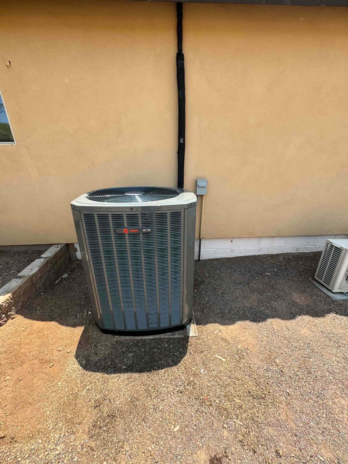 New outdoor heat pump condenser set on a level pad with insulated line set and weatherproof disconnect mounted on the wall.