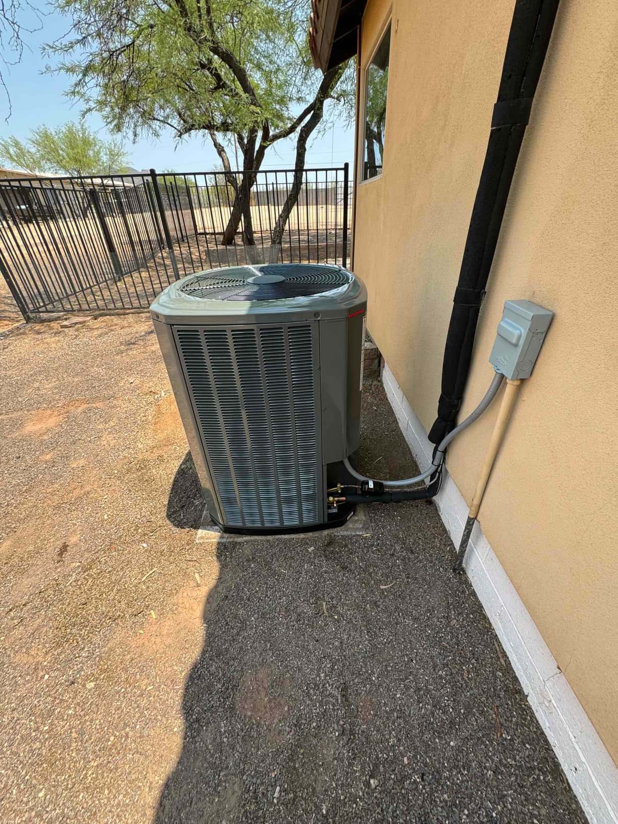 New outdoor heat pump condenser set on a level pad with insulated line set and electrical disconnect installed at the wall.