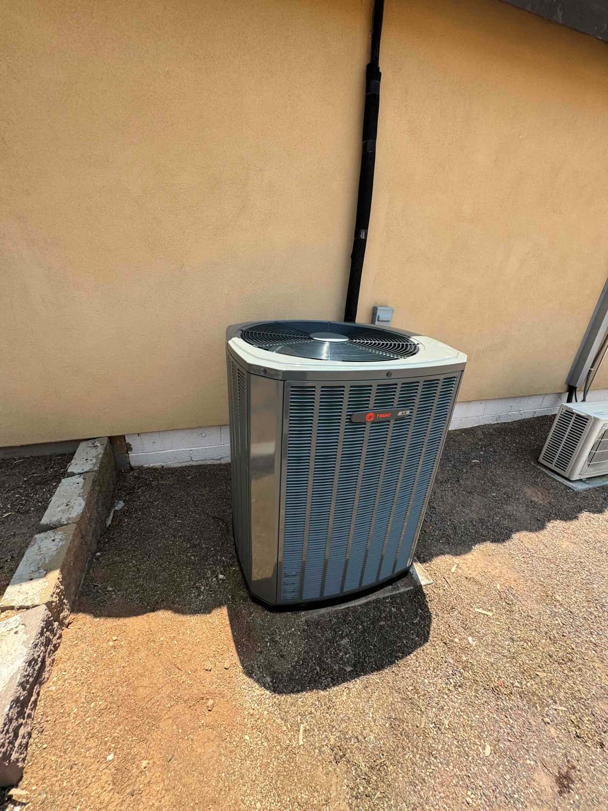 New outdoor heat pump condenser set on a level pad with insulated line set secured to the wall.
