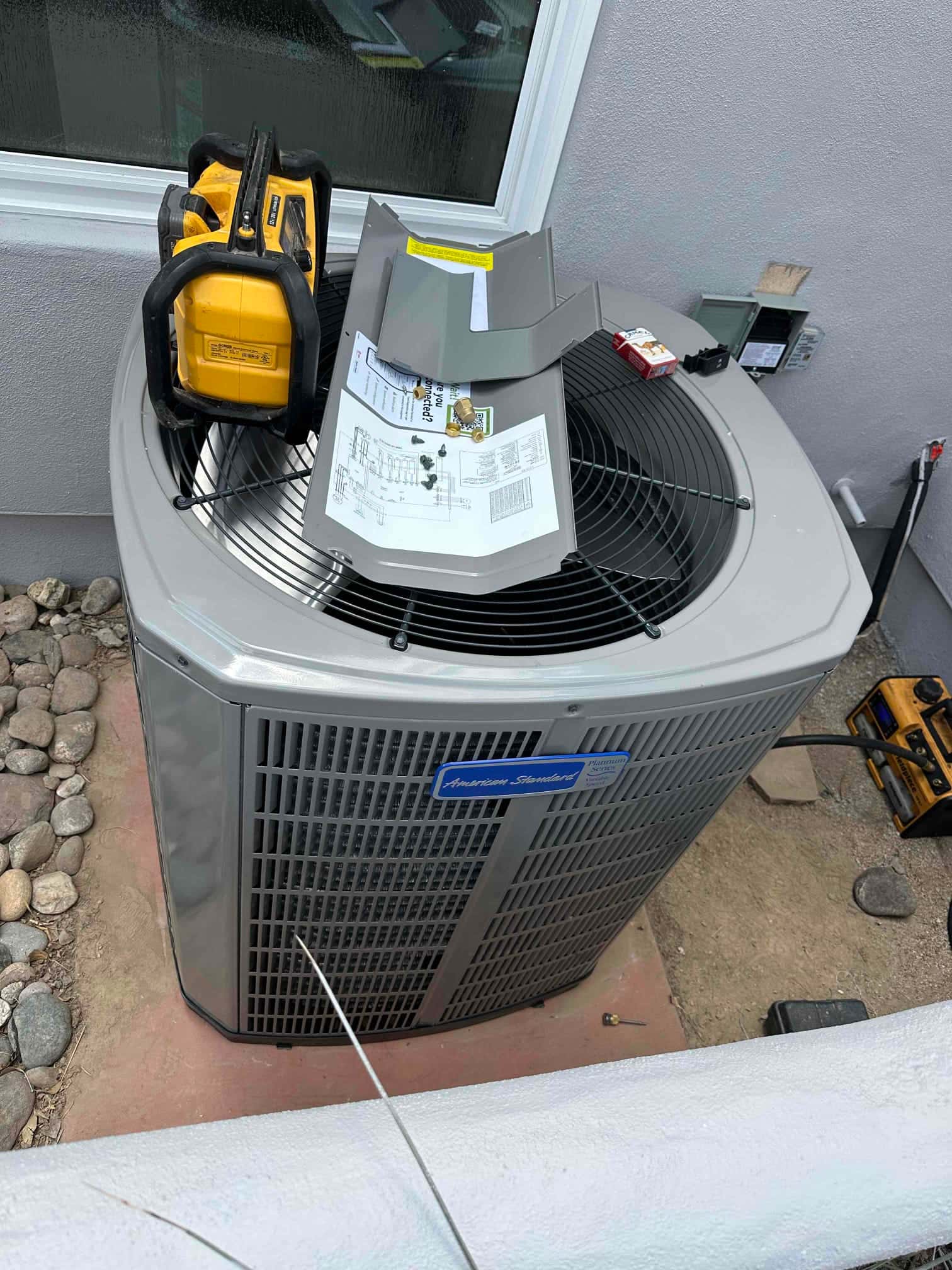 New outdoor heat pump condenser set on a level pad with tools and panel parts staged on top during installation.