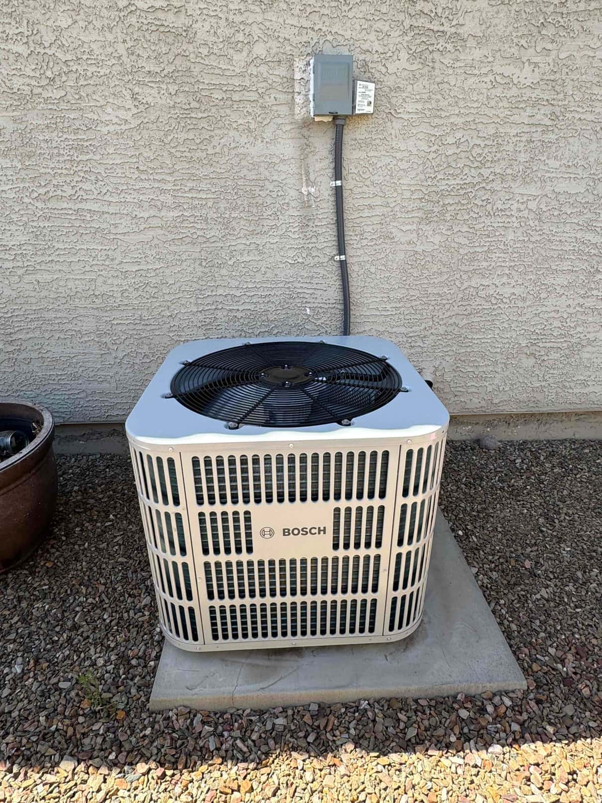 New outdoor heat pump condenser set on a level pad with weatherproof disconnect and sealed conduit mounted on the wall.
