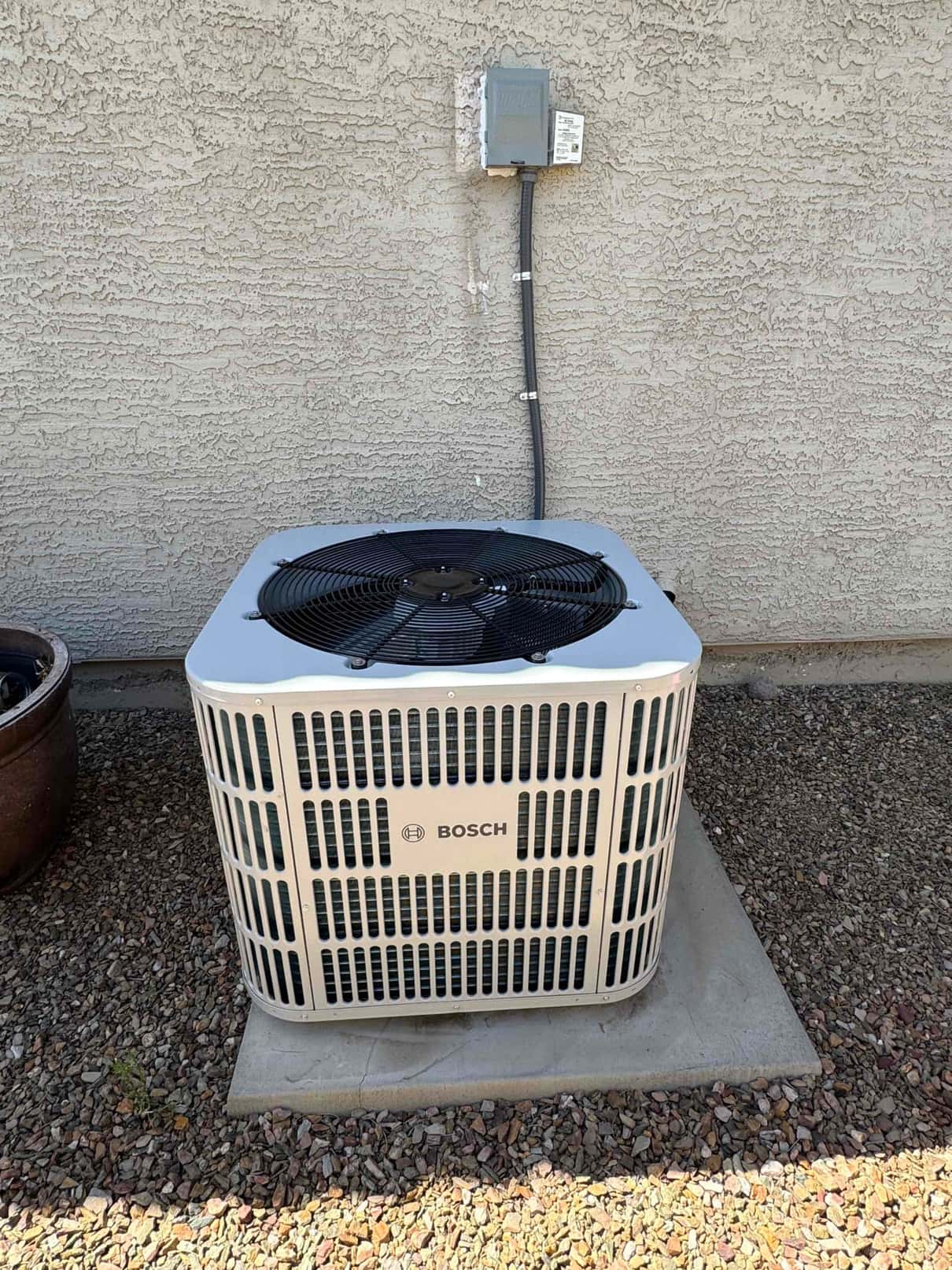 New outdoor heat pump condenser set on a level pad with weatherproof disconnect and conduit mounted on the exterior wall.