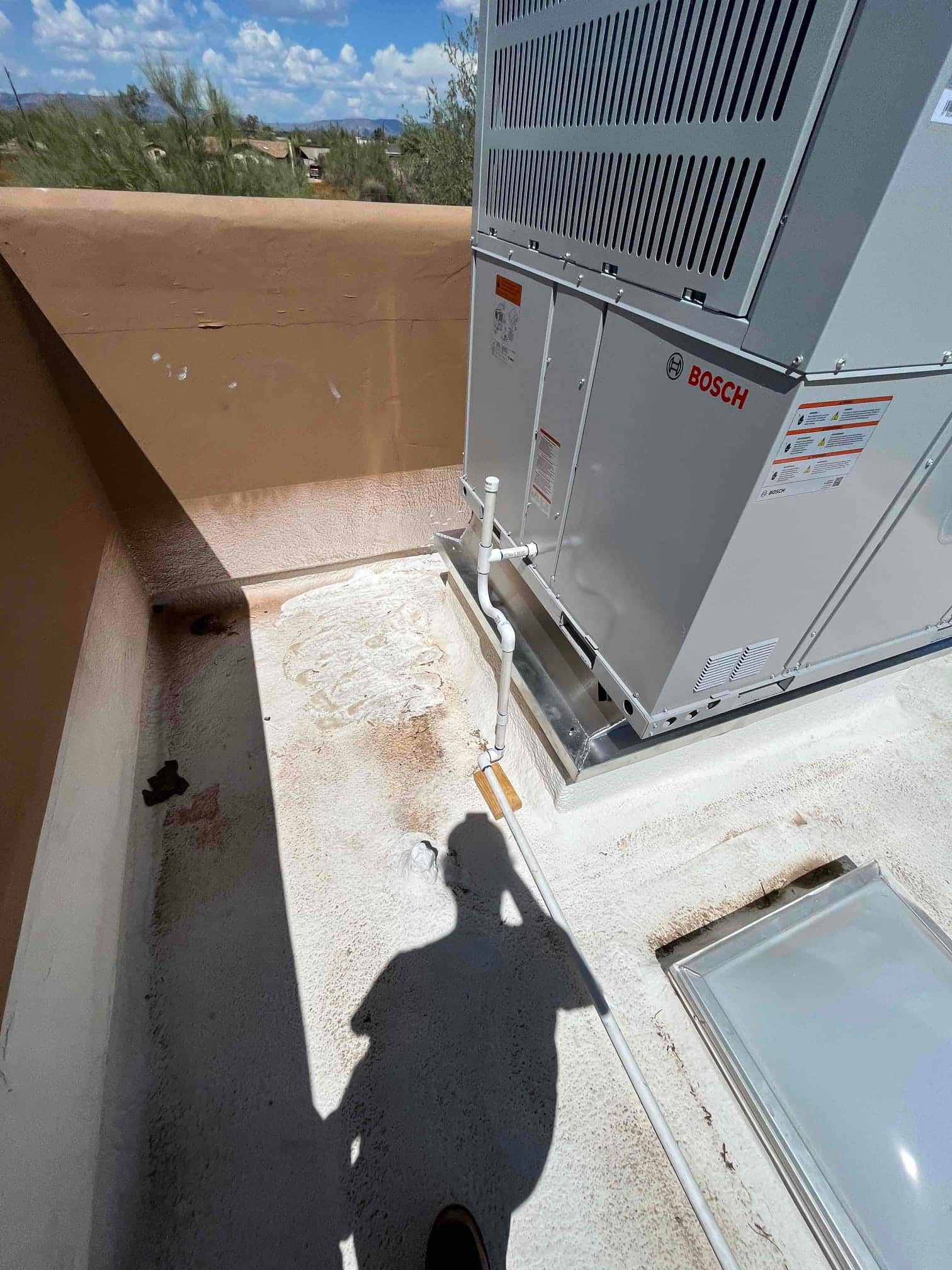 New rooftop heat pump set on a curb with routed condensate drain and sealed roof penetration, photographed after installation.
