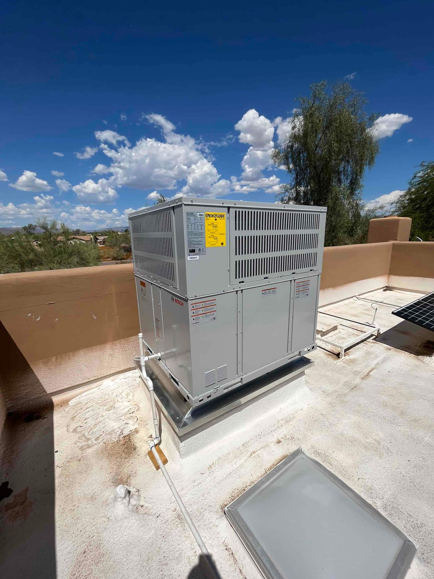 New rooftop packaged HVAC unit installed on a curb with connected condensate drain and sealed roof penetration.