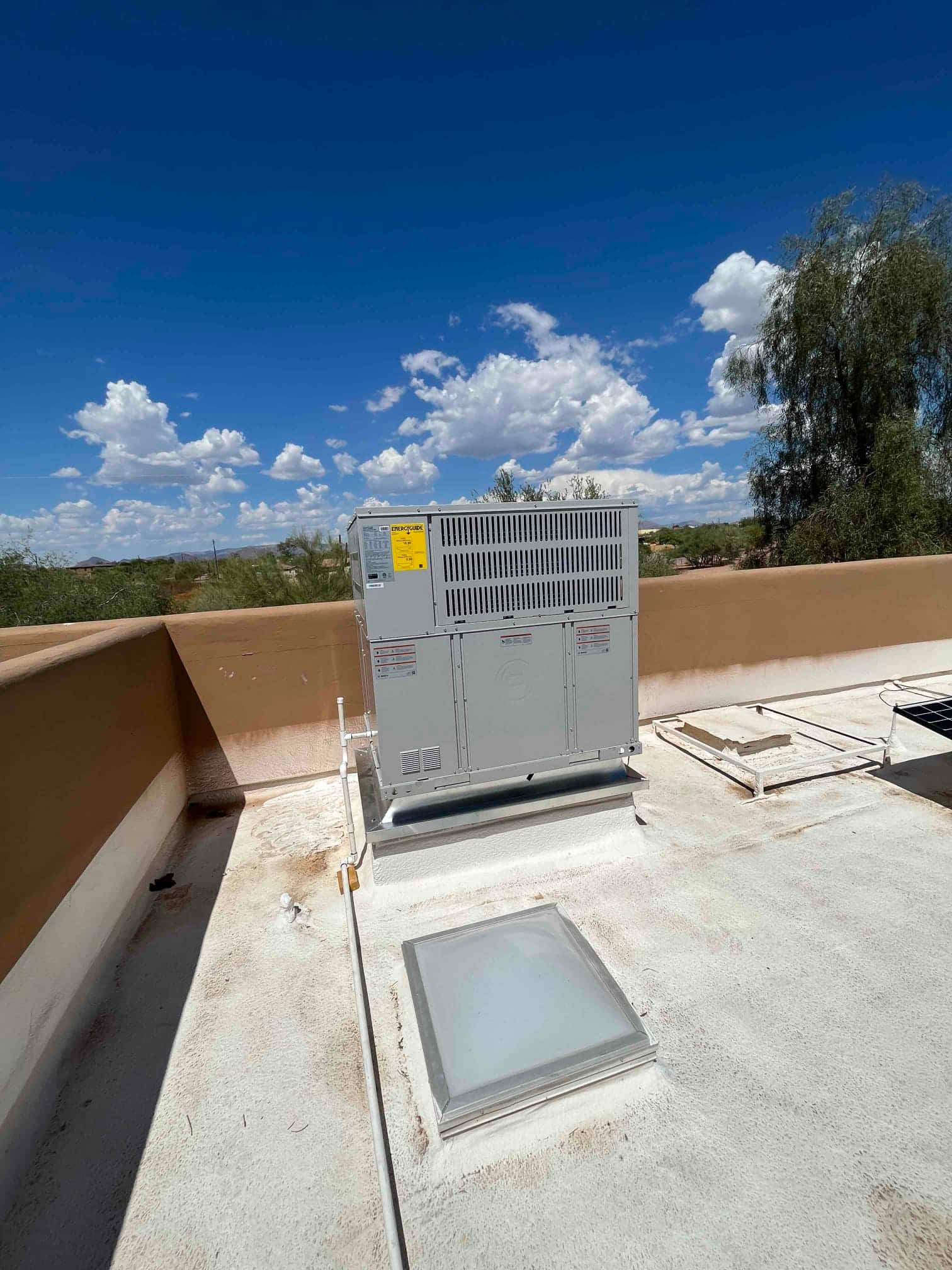 New rooftop packaged HVAC unit set on a curb with connected condensate drain and sealed roof penetration under clear skies.