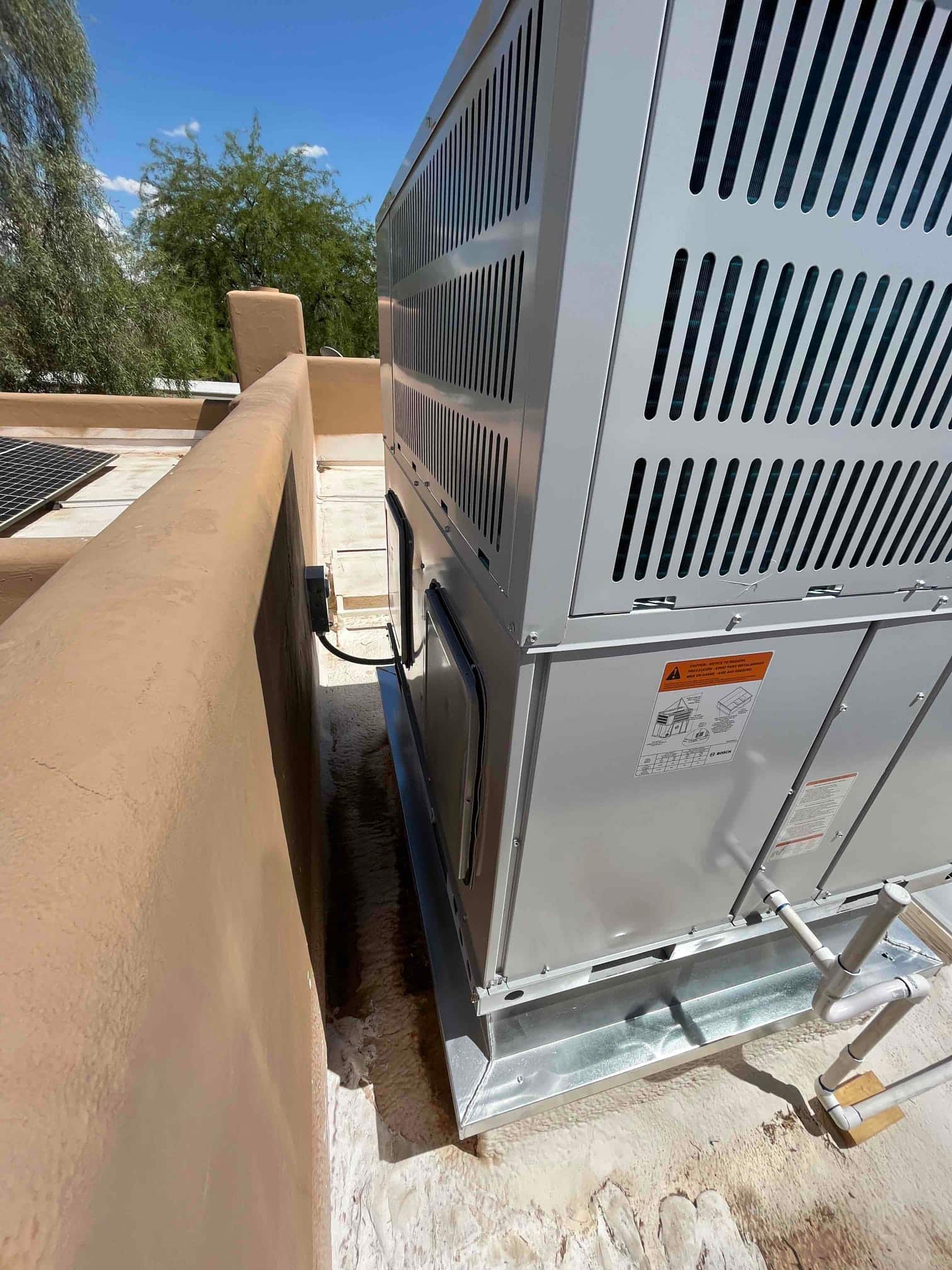 New rooftop packaged HVAC unit set on a metal curb with connected condensate drain piping and sealed roof surface.