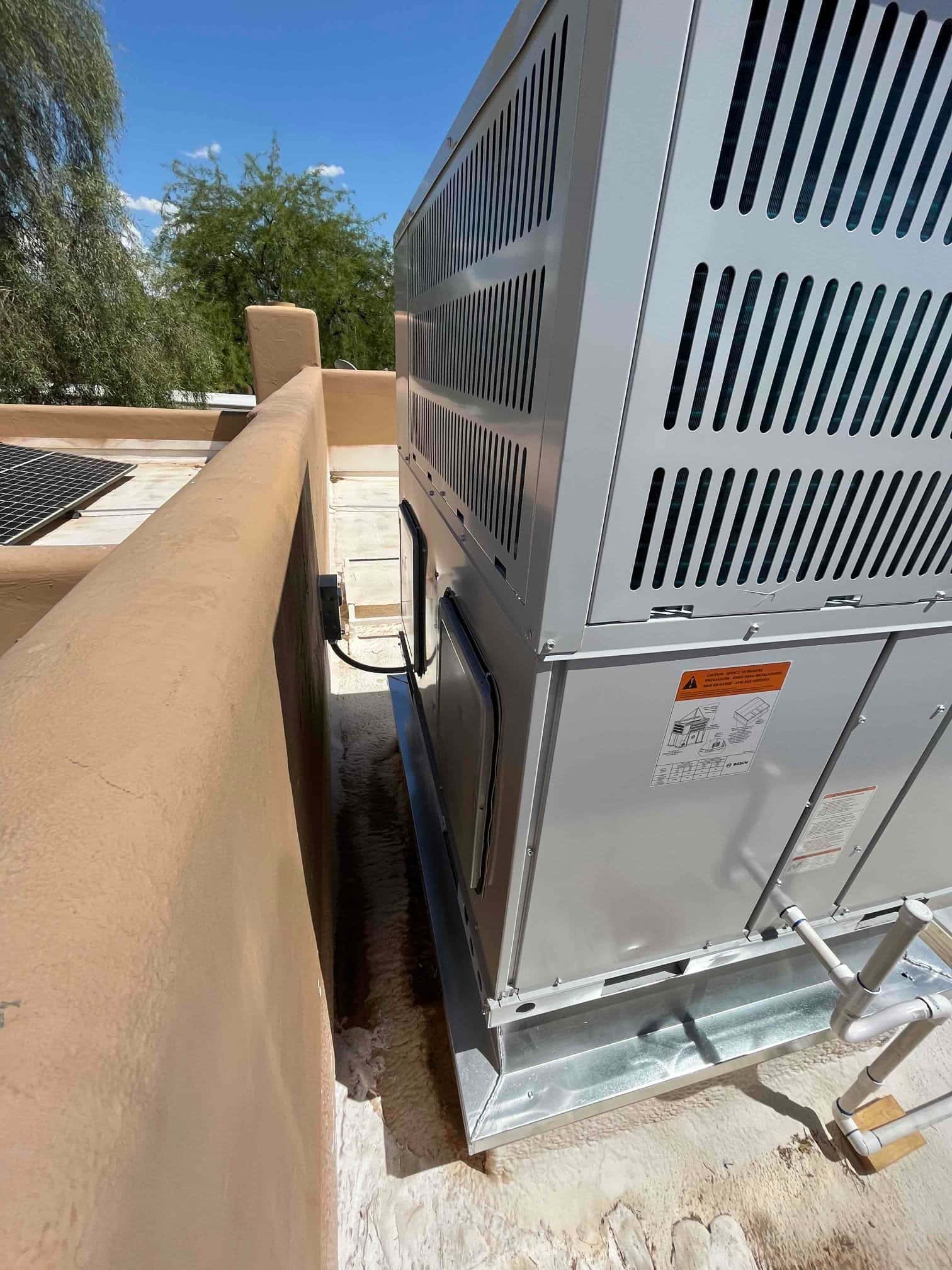 New rooftop packaged HVAC unit set on a raised curb with connected condensate drain and sealed roof surface.