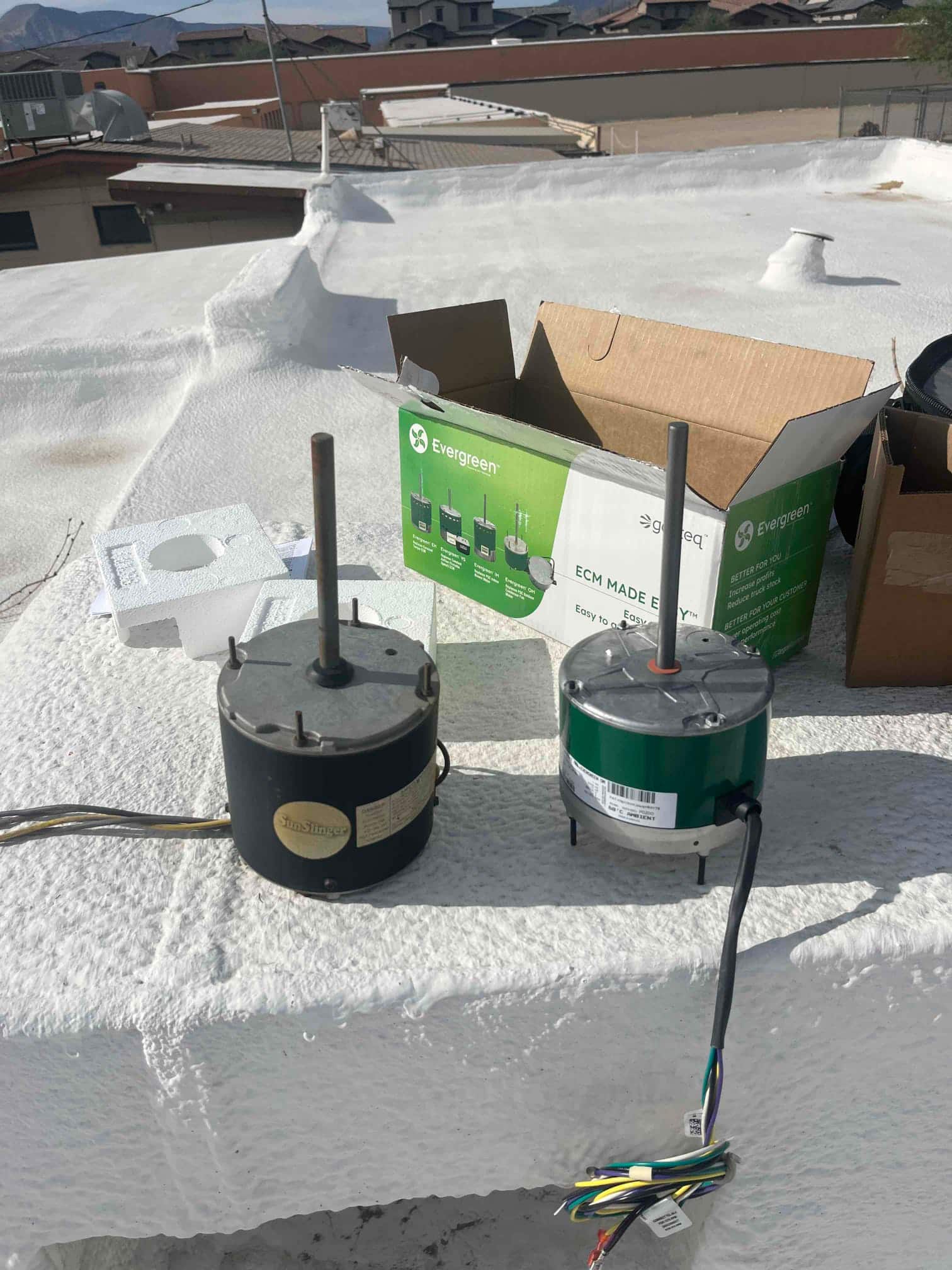 Old condenser fan motor removed next to new ECM replacement on a rooftop unit, with wiring harness and packaging visible.