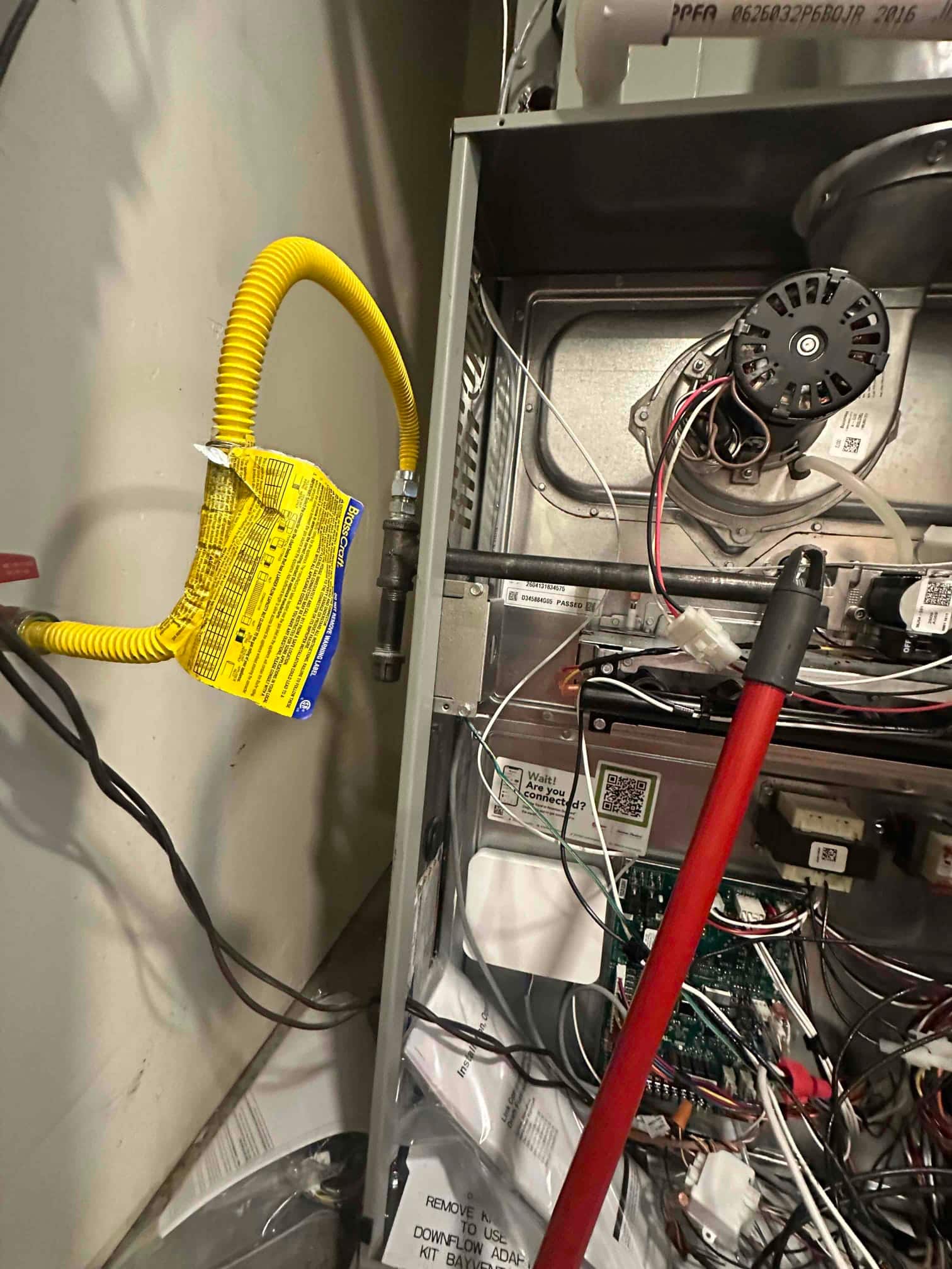 Open furnace cabinet shows new gas flex connector, induced draft motor, control board wiring, and PVC venting during installation.