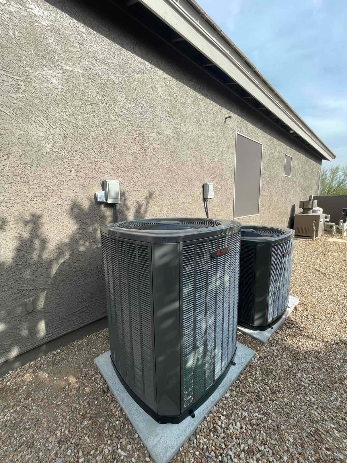 Two outdoor air conditioning condensers set on level pads with disconnects mounted on the wall and insulated line sets.