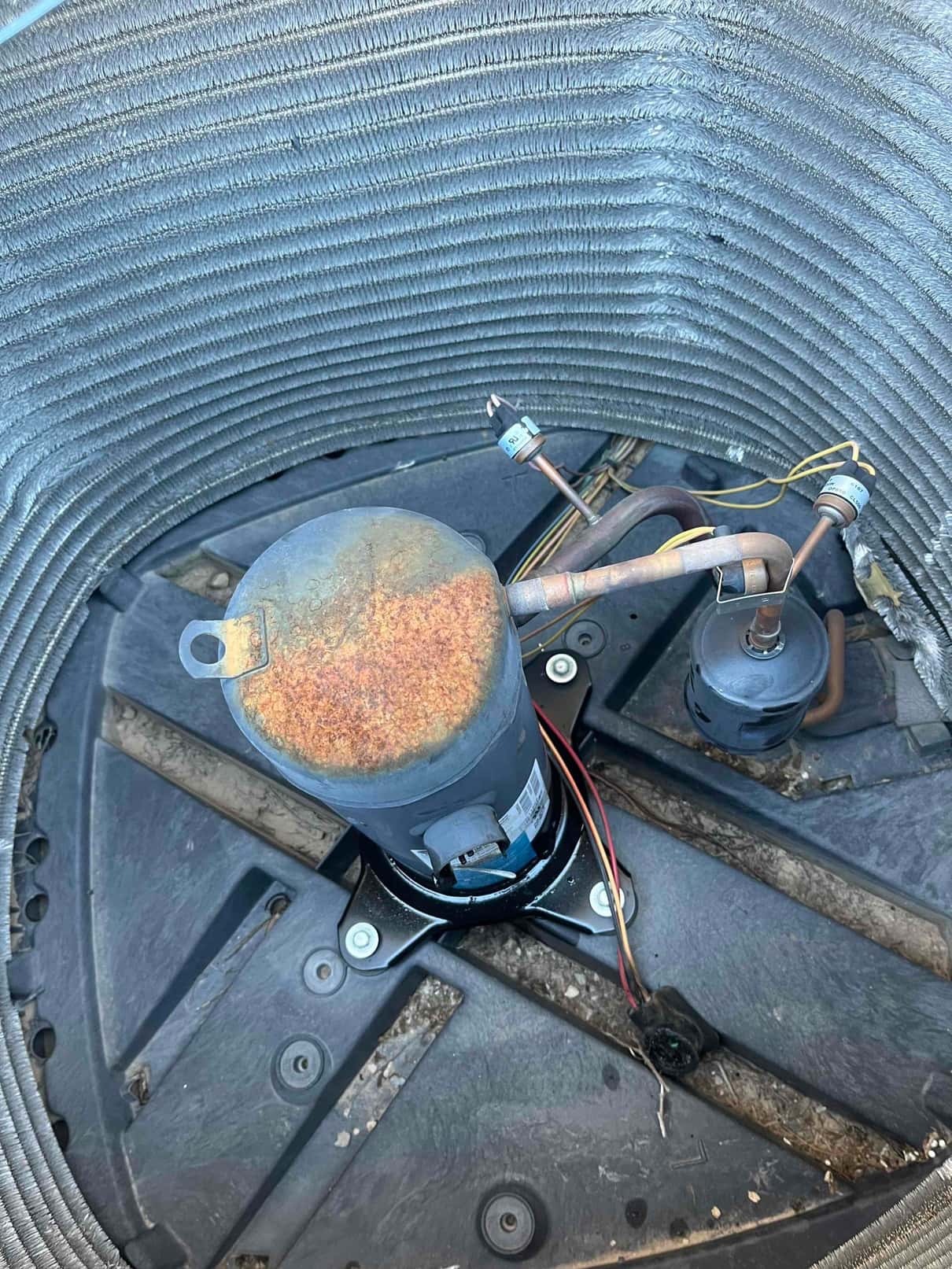 Outdoor condenser cabinet opened, showing rusted compressor shell and bi-flow filter drier connected to copper refrigerant lines.