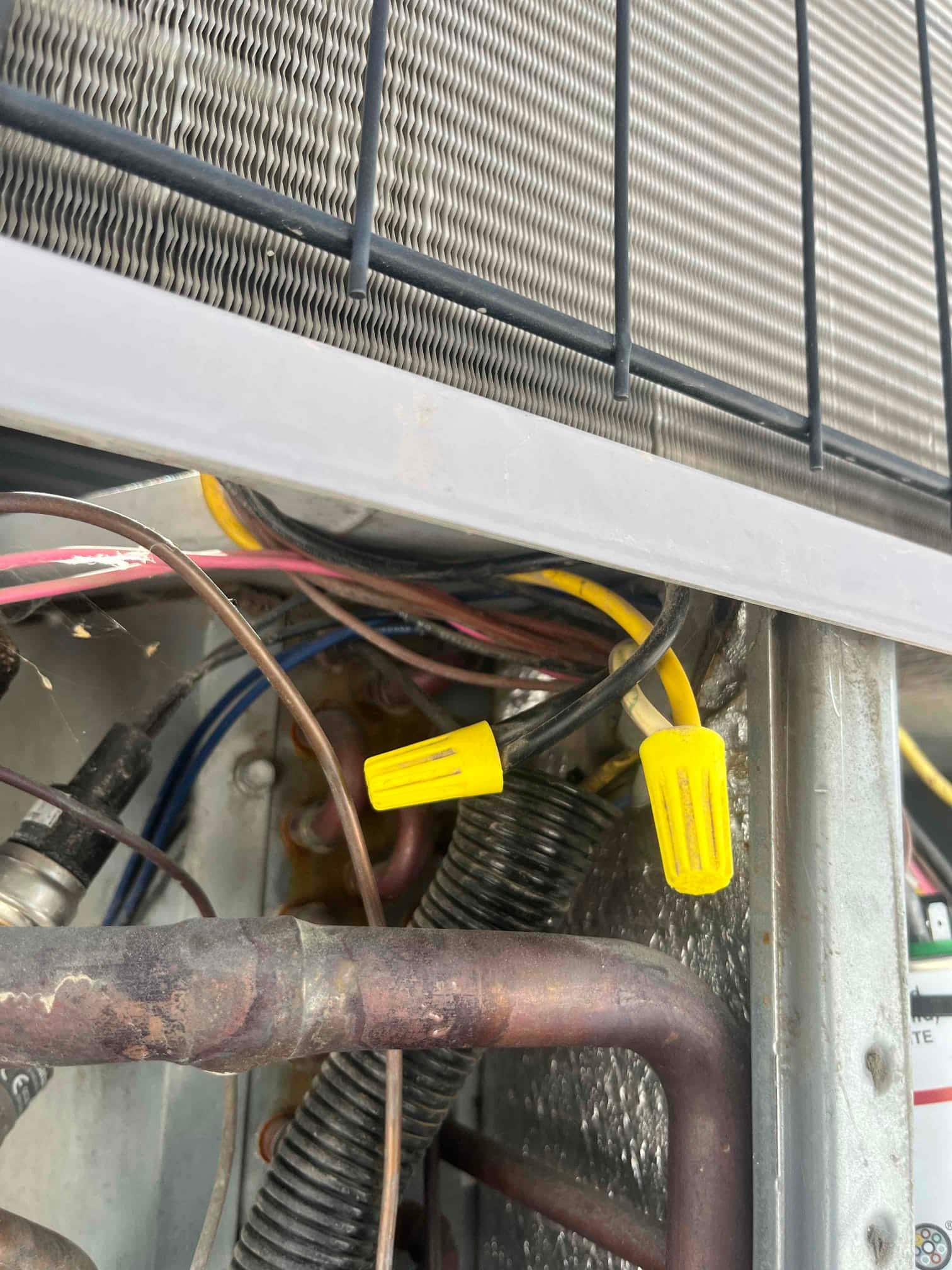 Outdoor condenser compartment showing yellow wire connectors on motor leads, condenser coil tubing, and wiring near the fan section.