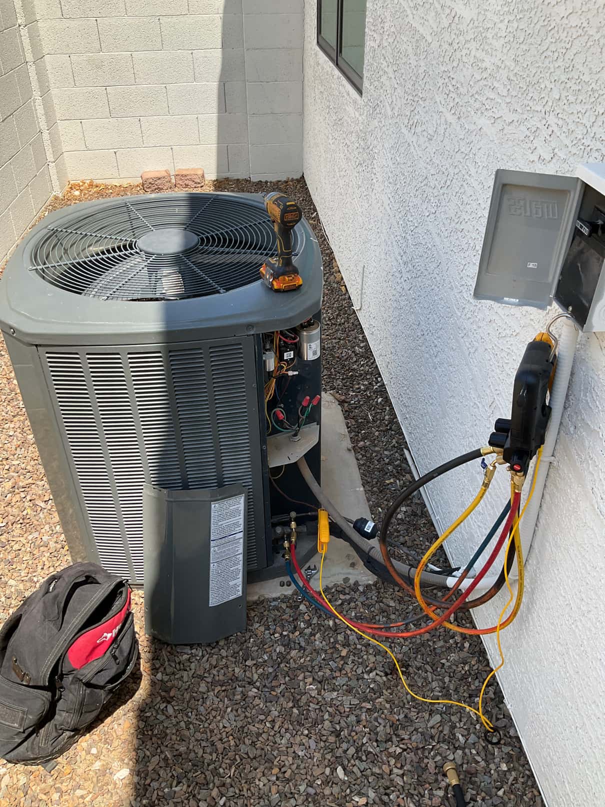 Outdoor condenser with service panel open; manifold gauge hoses connected at service ports near the disconnect.