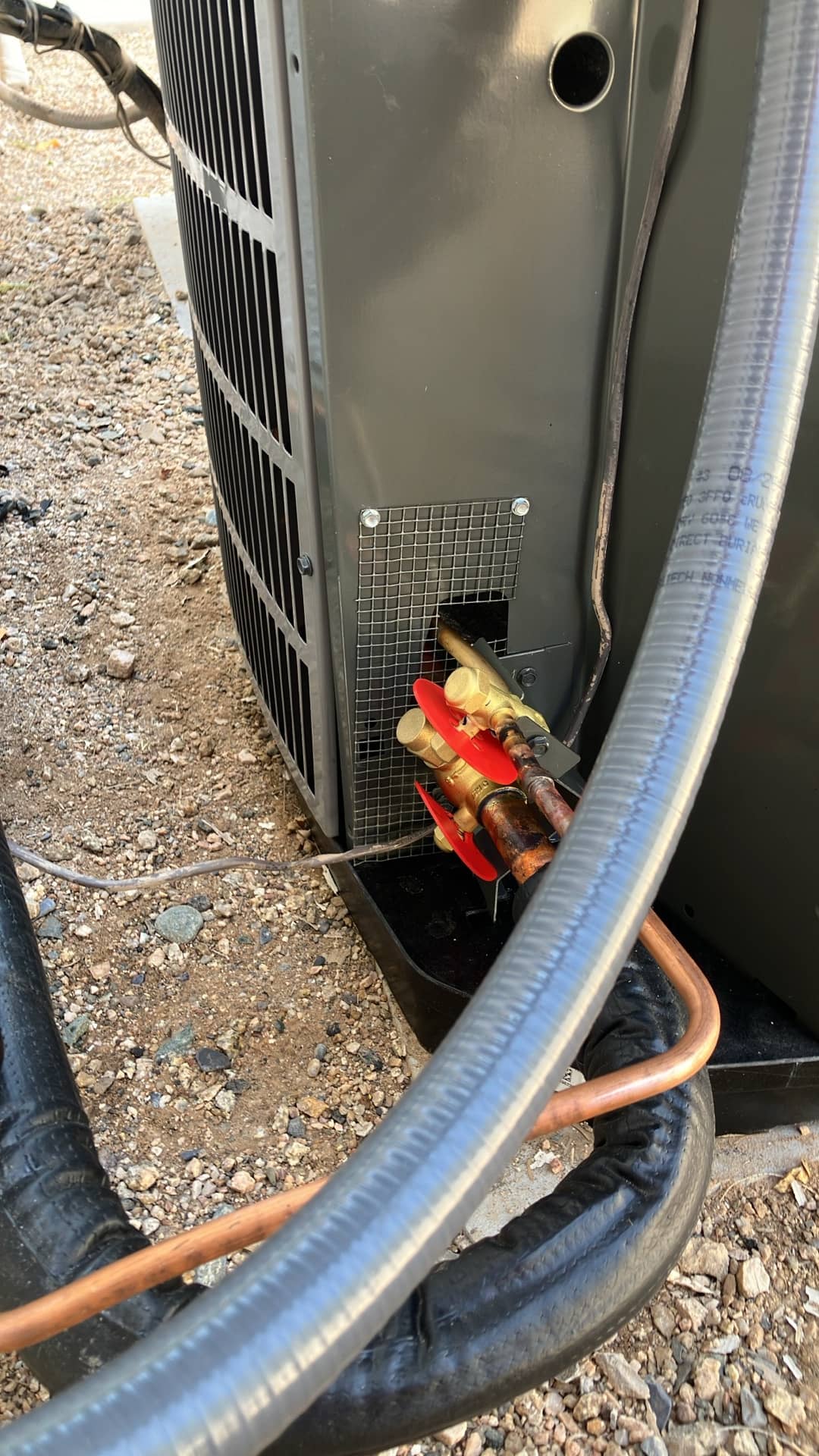 Outdoor condenser service valves with red caps and newly connected insulated refrigerant lines routed to the unit.