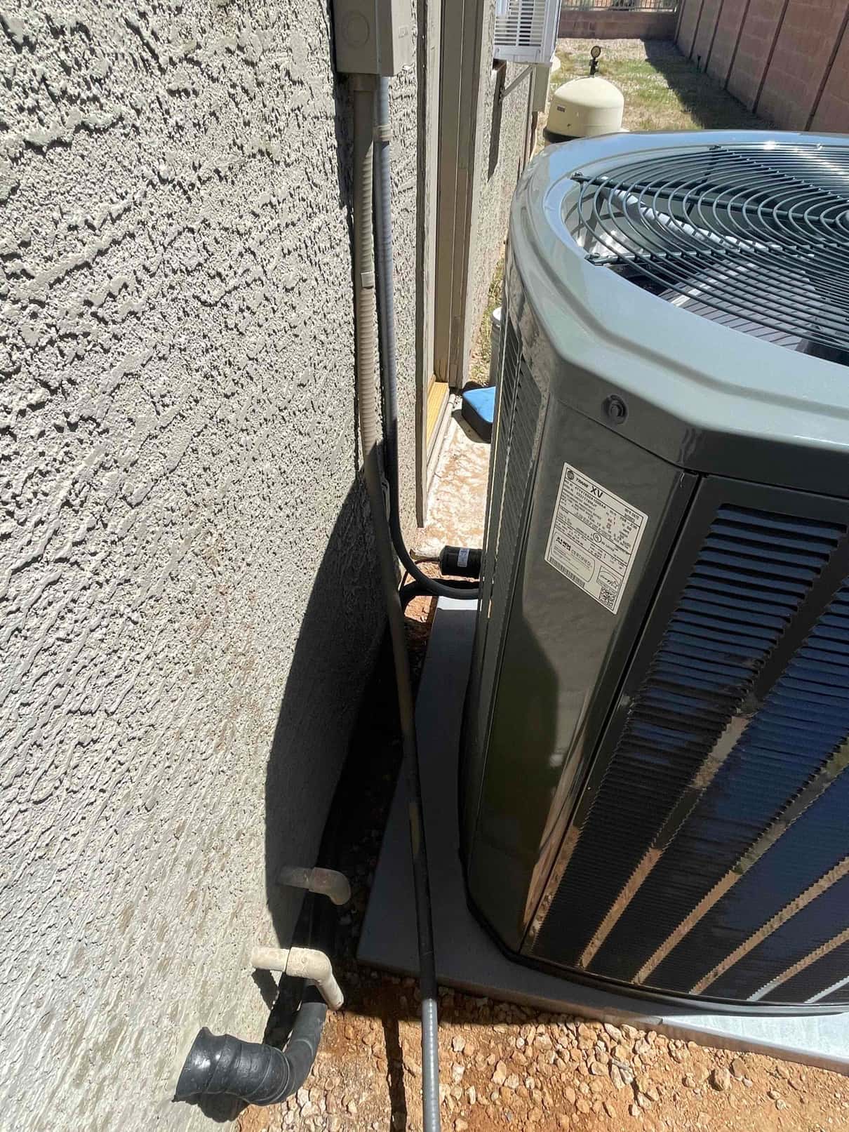 Outdoor condenser set on a level pad with insulated refrigerant line set, electrical whip, and wall-mounted disconnect.
