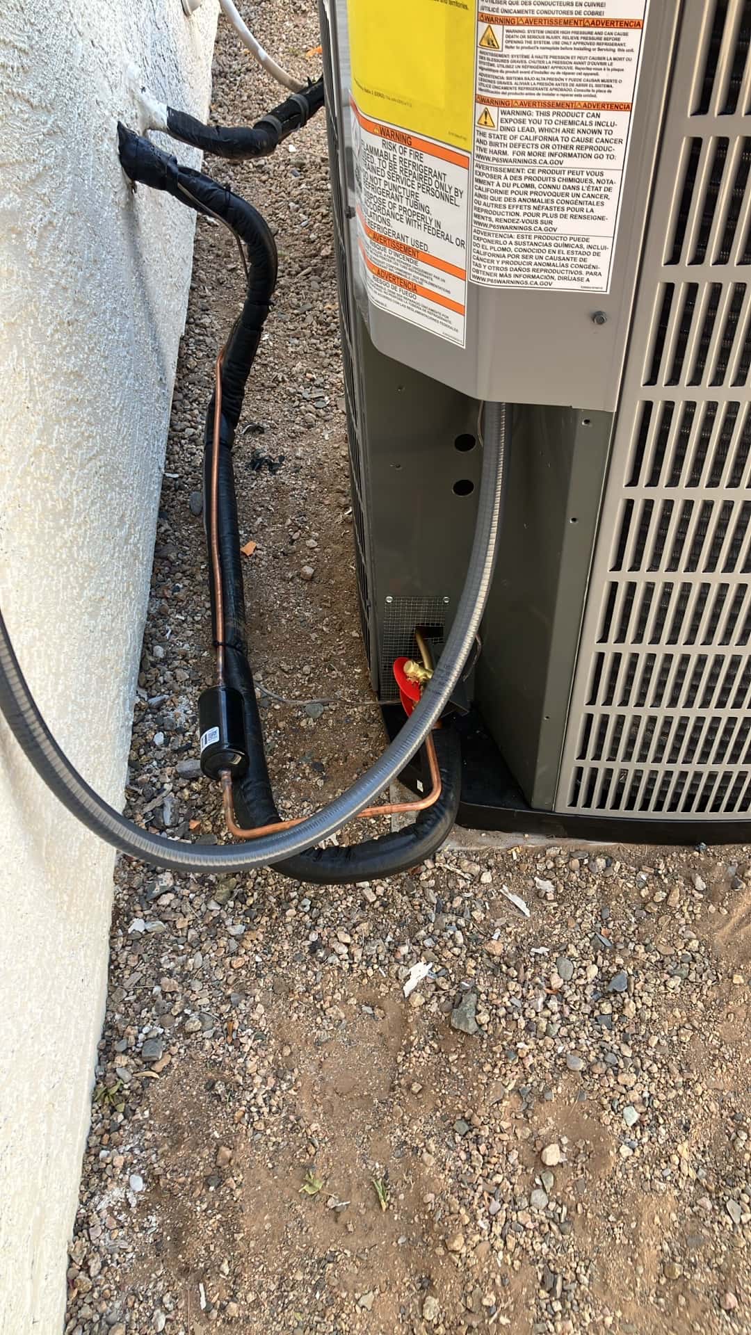 Outdoor condenser set on a pad with insulated refrigerant lines, filter-drier, and sealed wall penetration routed to the unit.