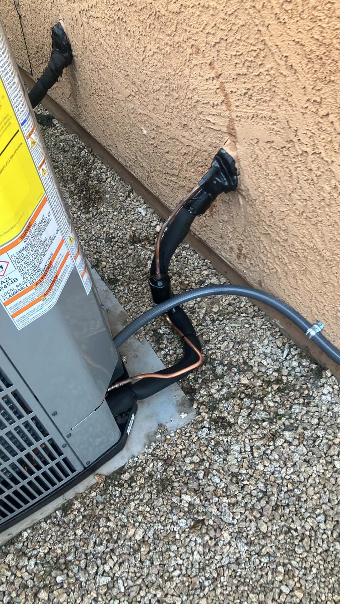 Outdoor condenser set on a pad with insulated refrigerant lines and flexible electrical whip secured to the stucco wall.