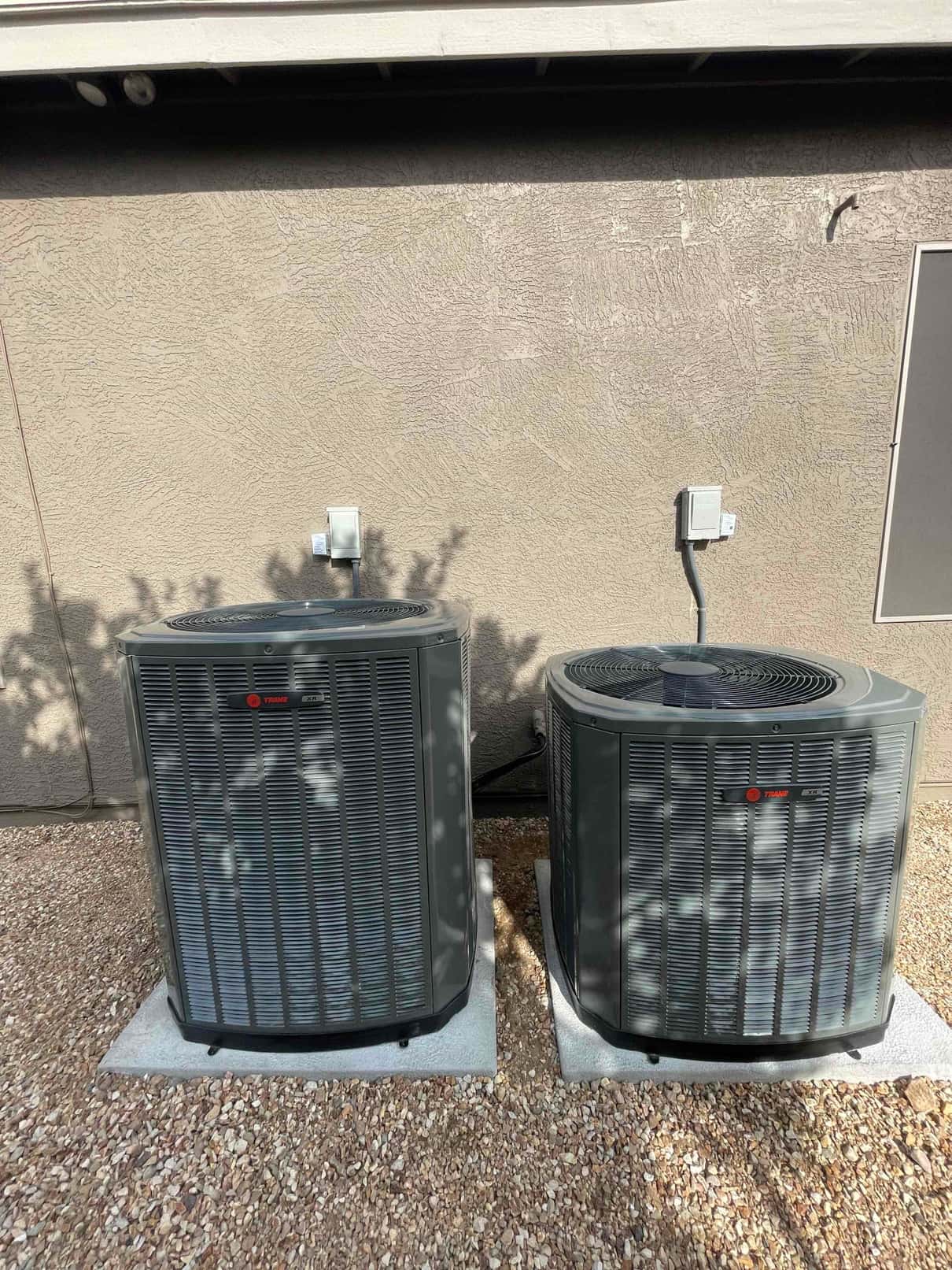 Two outdoor condensers set on level pads with electrical disconnects mounted on the wall and refrigerant lines connected.