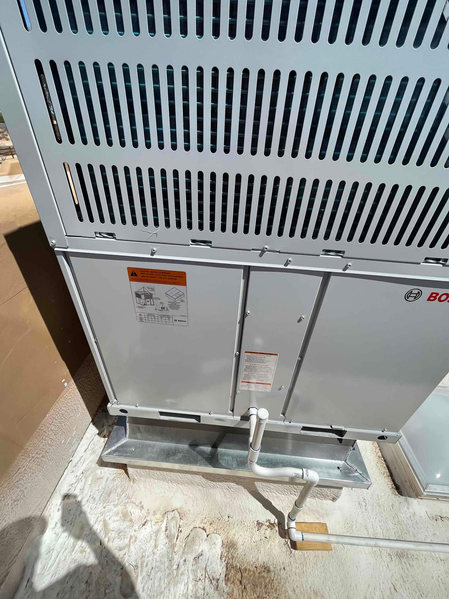Outdoor condensing unit set on a metal curb with PVC drain piping routed and secured on the rooftop surface.