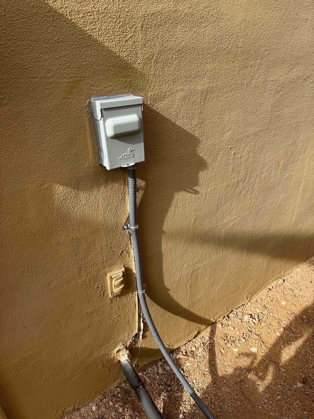 Outdoor HVAC disconnect and flexible conduit mounted on exterior wall with sealed penetrations and drain line exiting to grade.