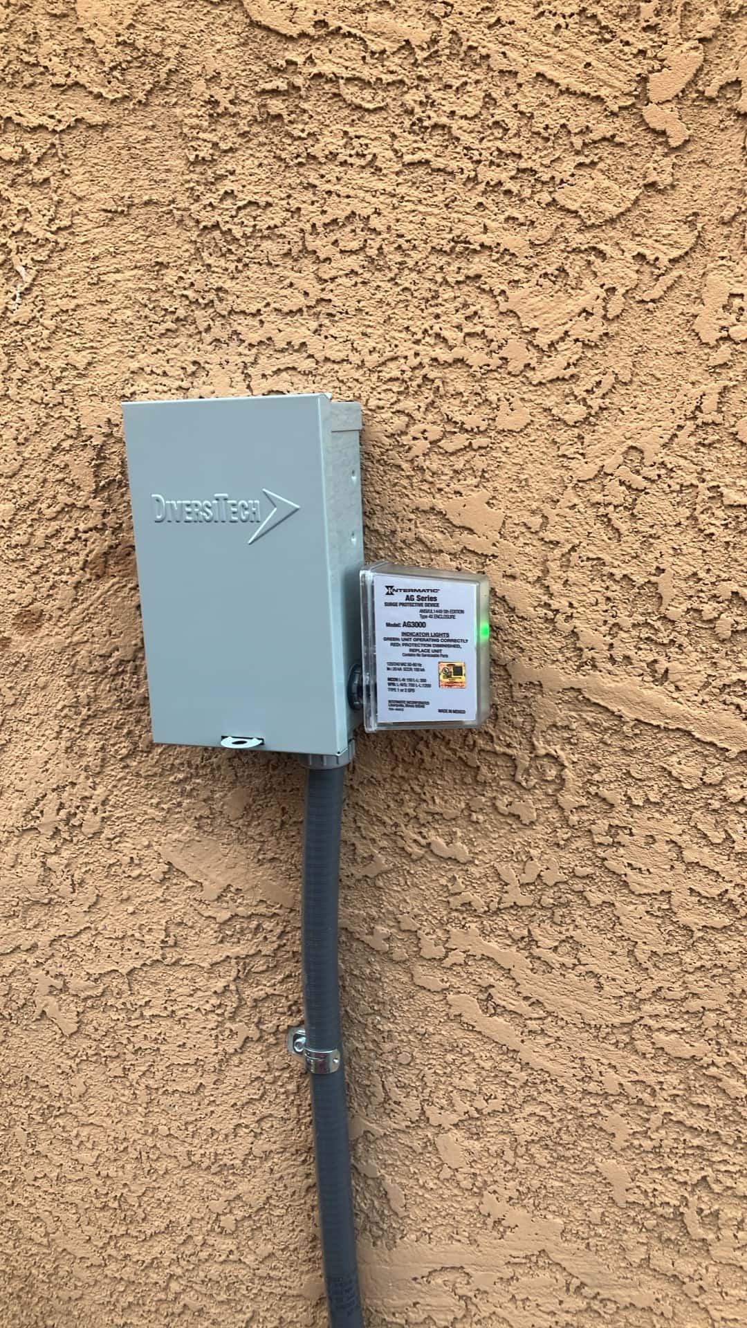 Outdoor HVAC disconnect with surge protector mounted on stucco wall, flexible conduit neatly secured with clamp and LED indicator illuminated.