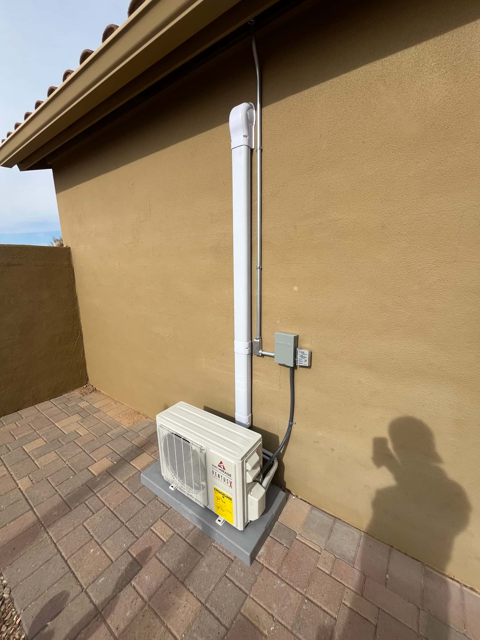 Outdoor mini-split condenser set on a level pad with line set cover, electrical conduit, and weatherproof disconnect mounted.