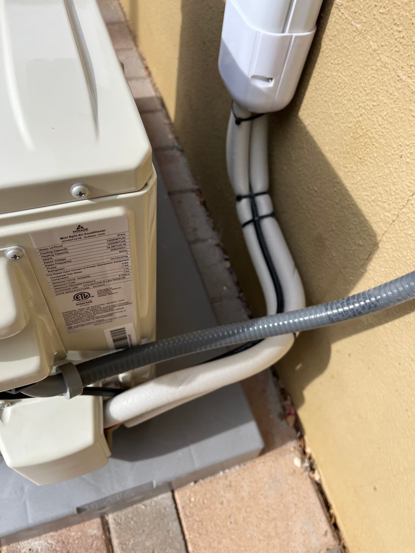 Outdoor mini-split condenser set on a pad with insulated line set in a cover and flexible electrical conduit routed to the unit.