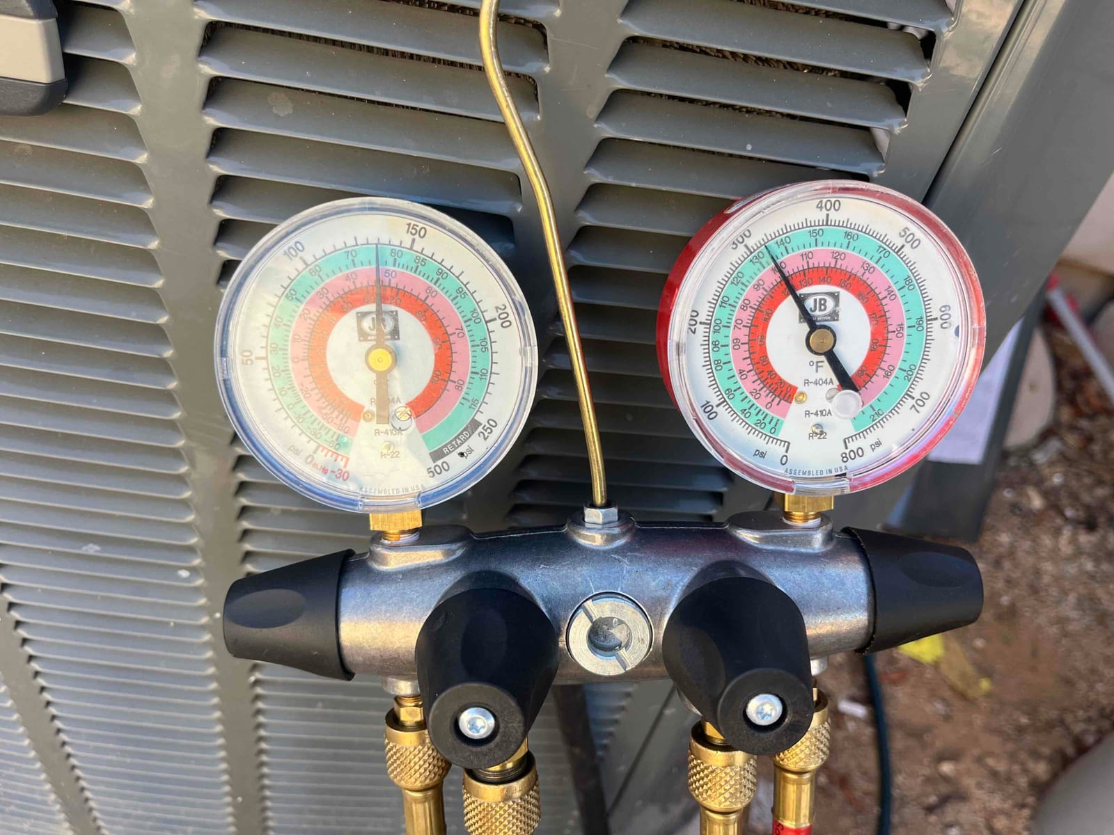 Refrigerant manifold gauges connected at the outdoor condenser service ports to check system pressures during air conditioning repair.