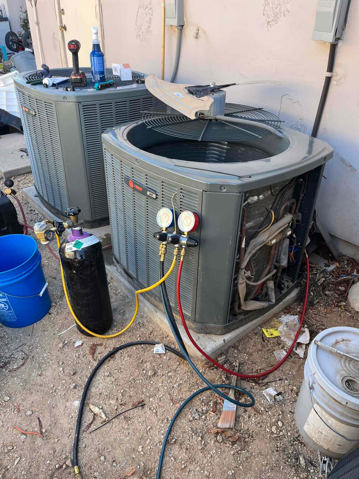 Refrigerant manifold gauges connected to the outdoor condenser during service, with recovery cylinder and service hoses arranged at the work area.