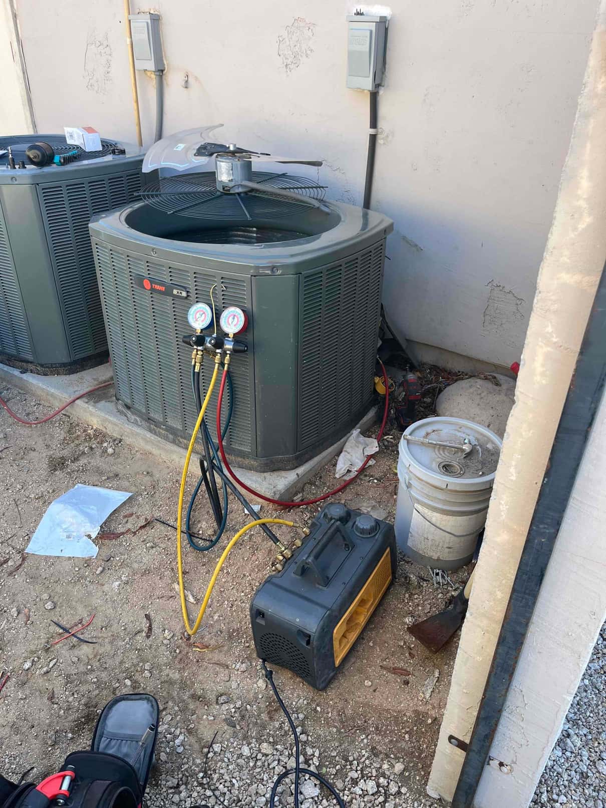 Refrigerant manifold gauges connected to an outdoor condenser during service, with a vacuum pump and hoses staged beside the unit.