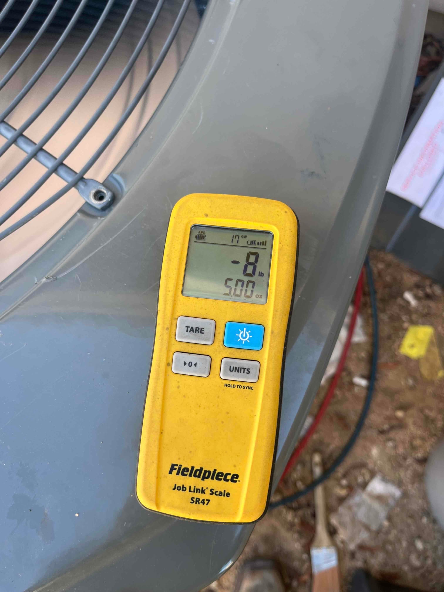 Refrigerant scale displays 5.00 lb while charging the outdoor condenser unit, with hoses connected at the service port.