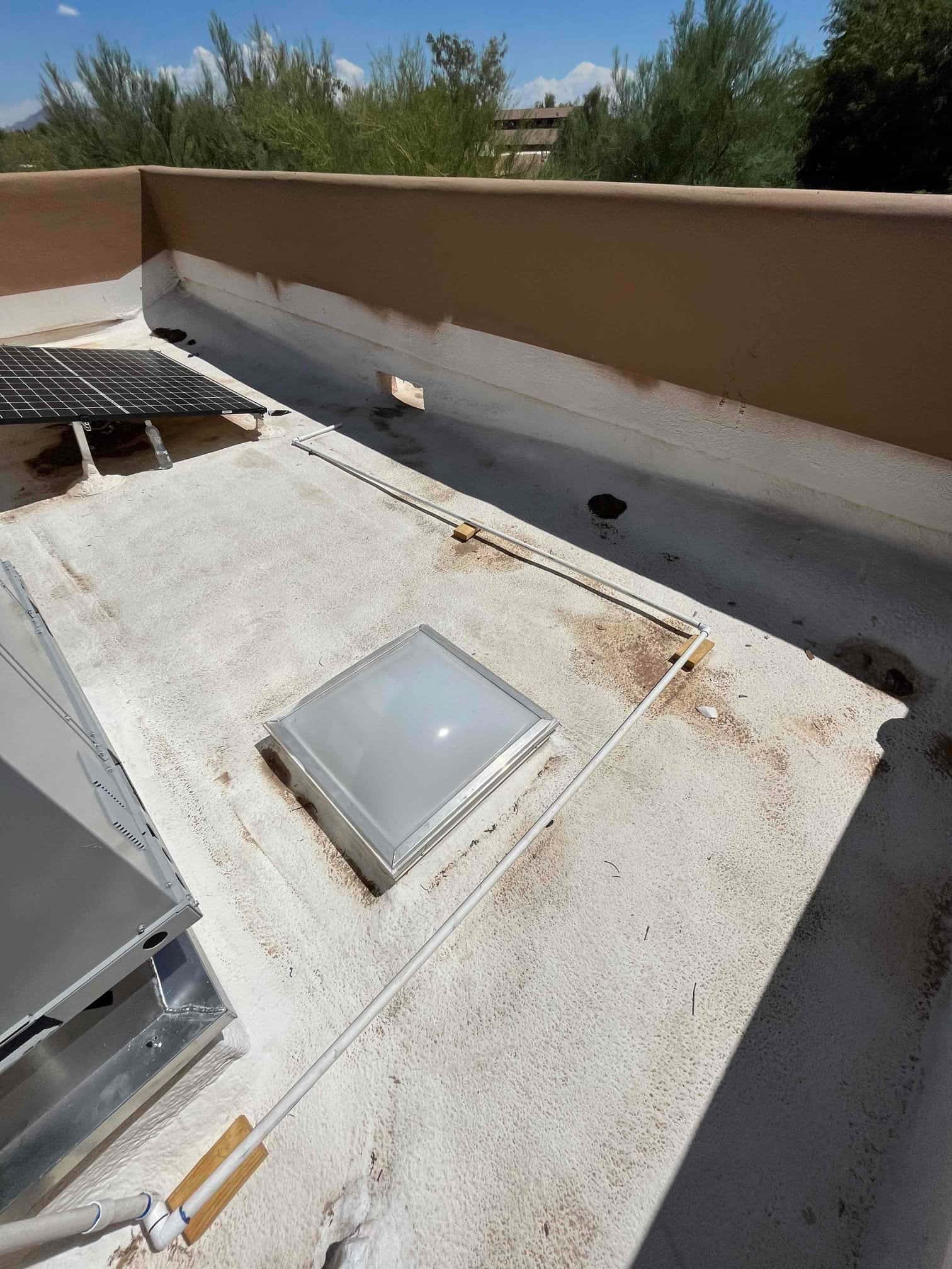 Rooftop installation area showing new condensate drain piping routed along the roof near a curb-mounted skylight.