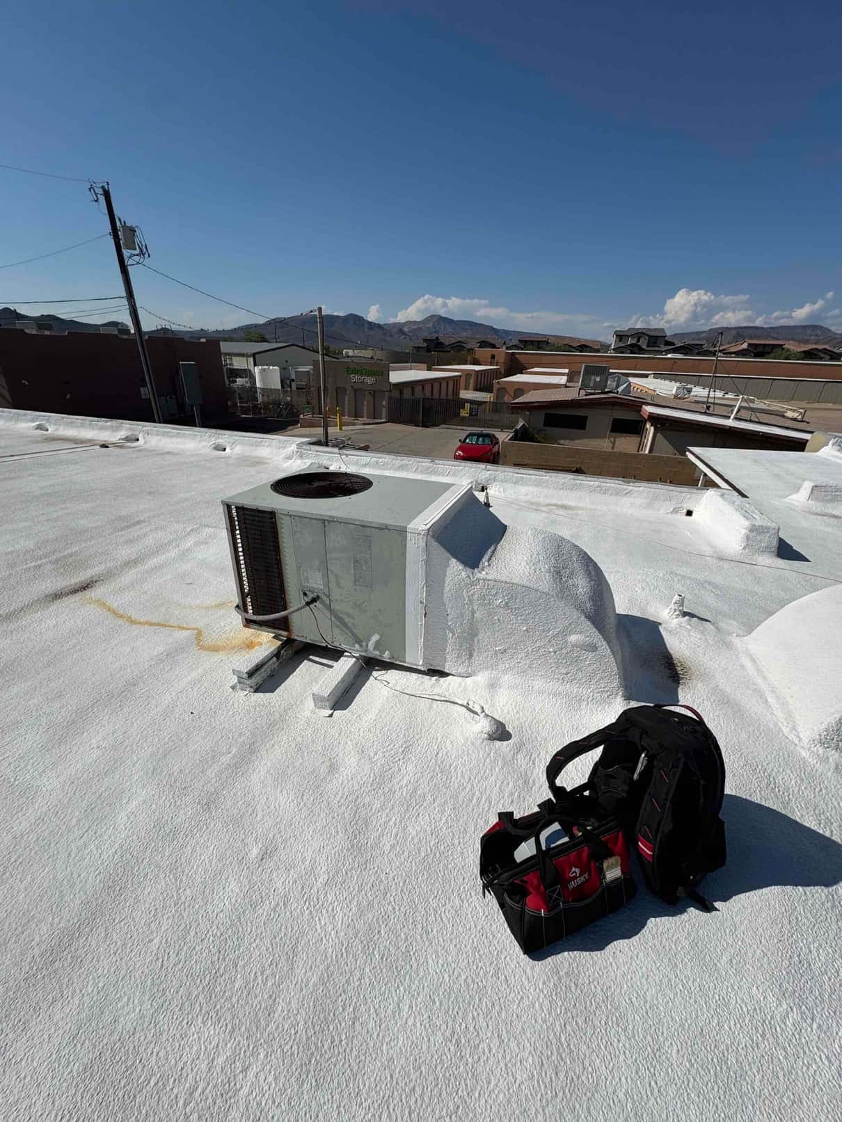 Rooftop package air conditioning unit with service panels open, showing wiring access beside technician’s tool bag and backpack.