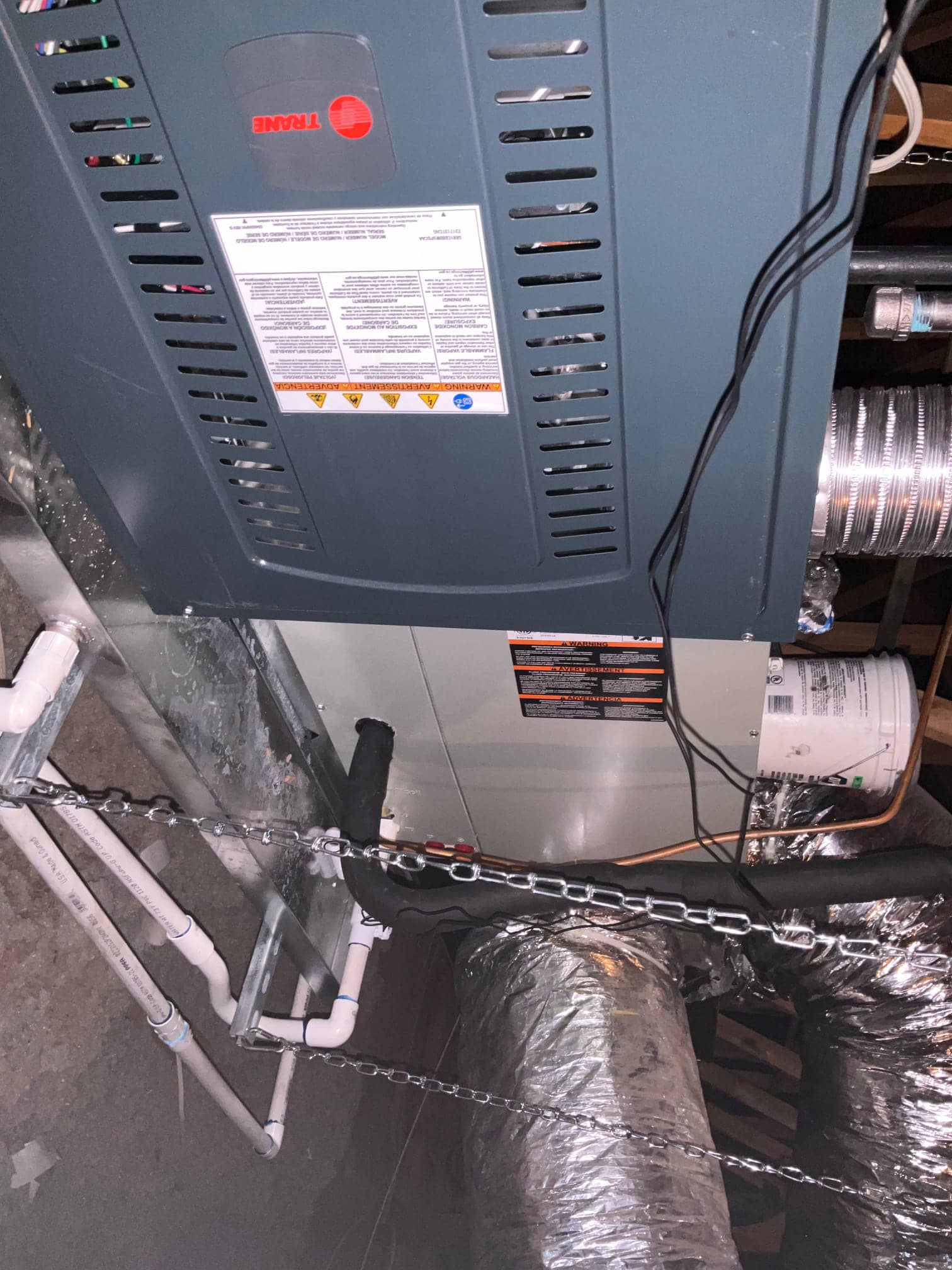 Suspended air handler and furnace installation with insulated refrigerant lines, flexible duct connections, and PVC condensate drain piping secured with hangers.