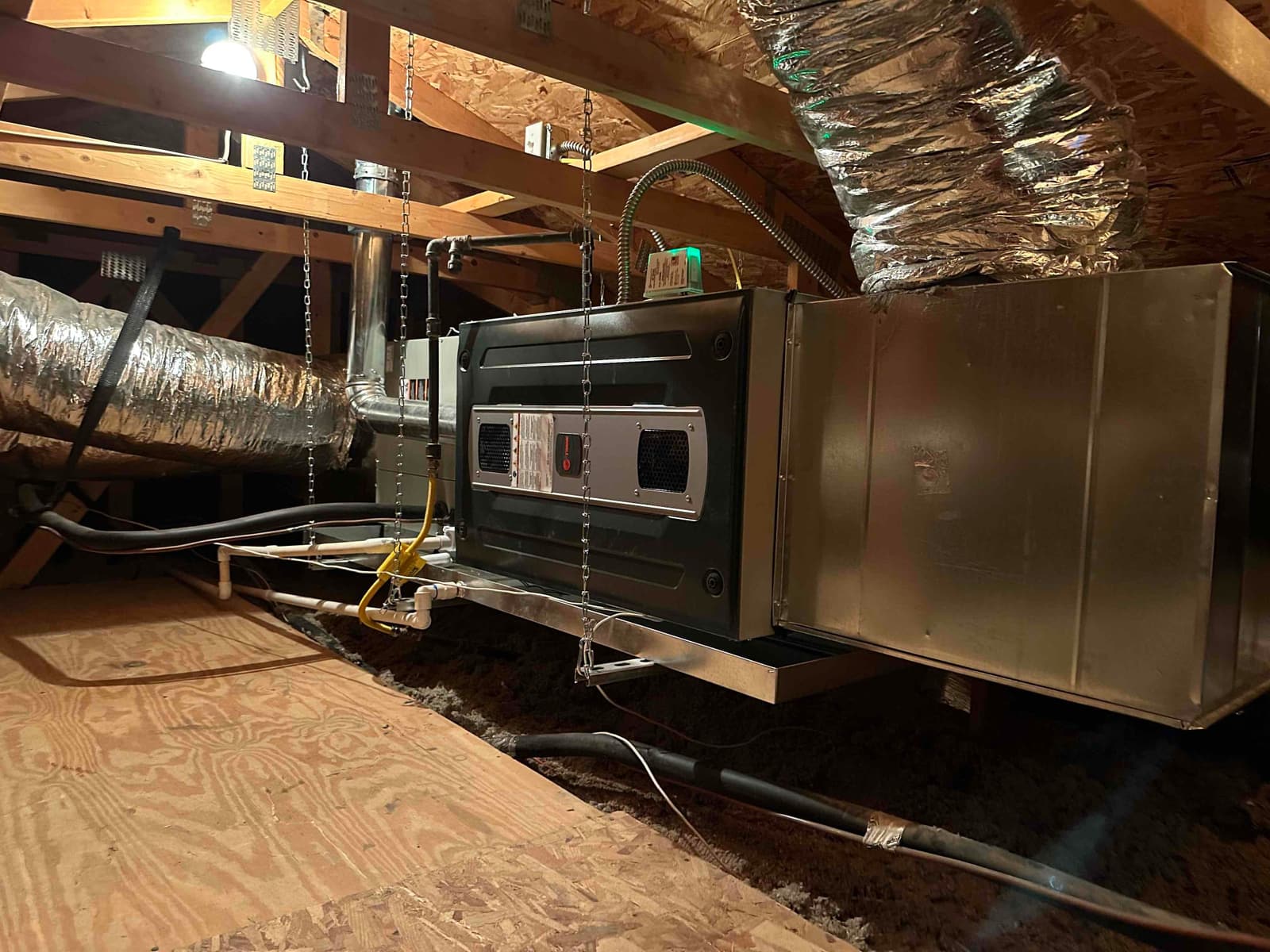 Suspended attic air handler and furnace installation with insulated duct connections, drain piping, and metal secondary drain pan beneath the unit.