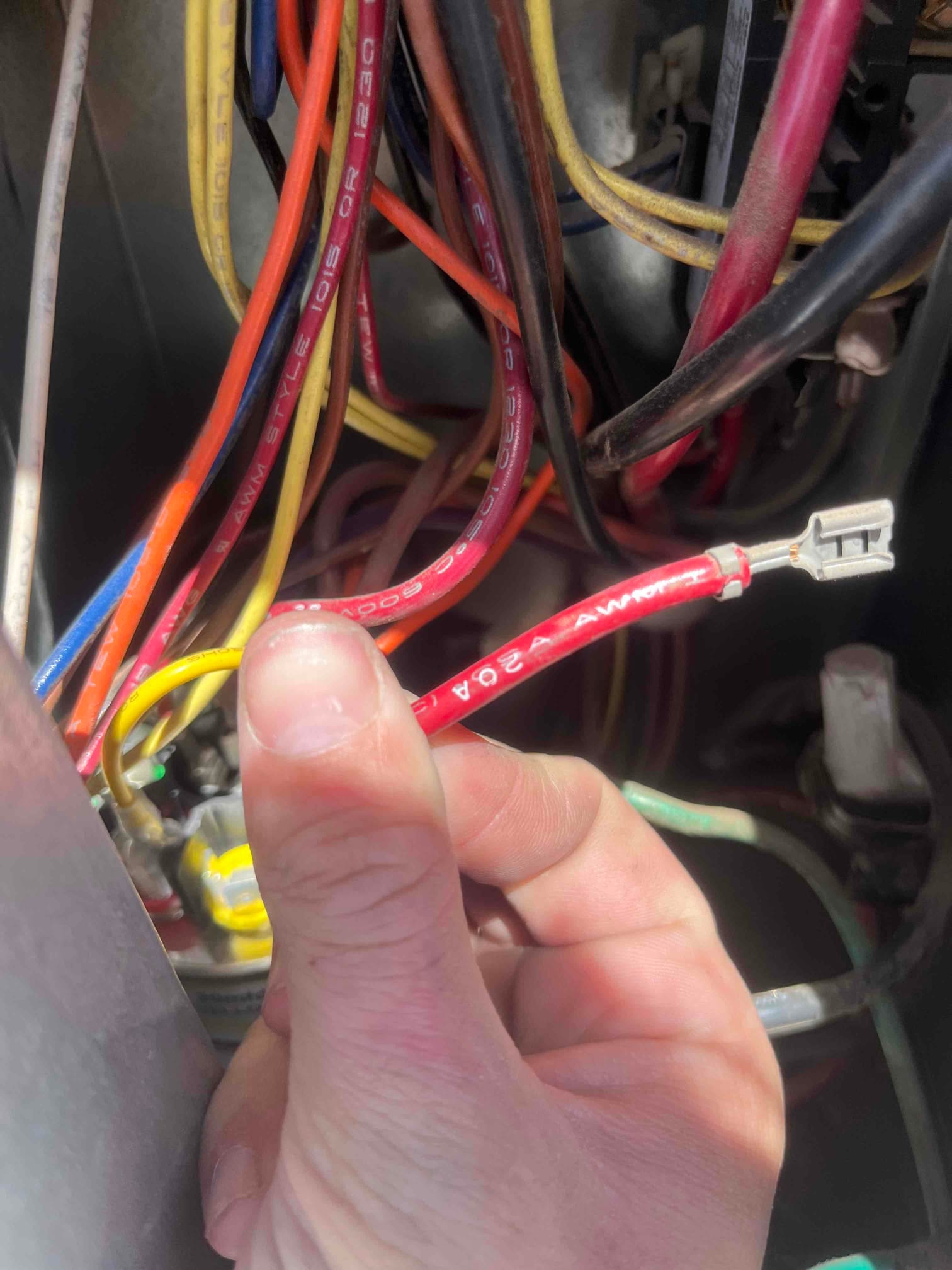 Technician holds a red 20A 300V insulated wire with spade terminal among condenser control wiring and capacitor leads.