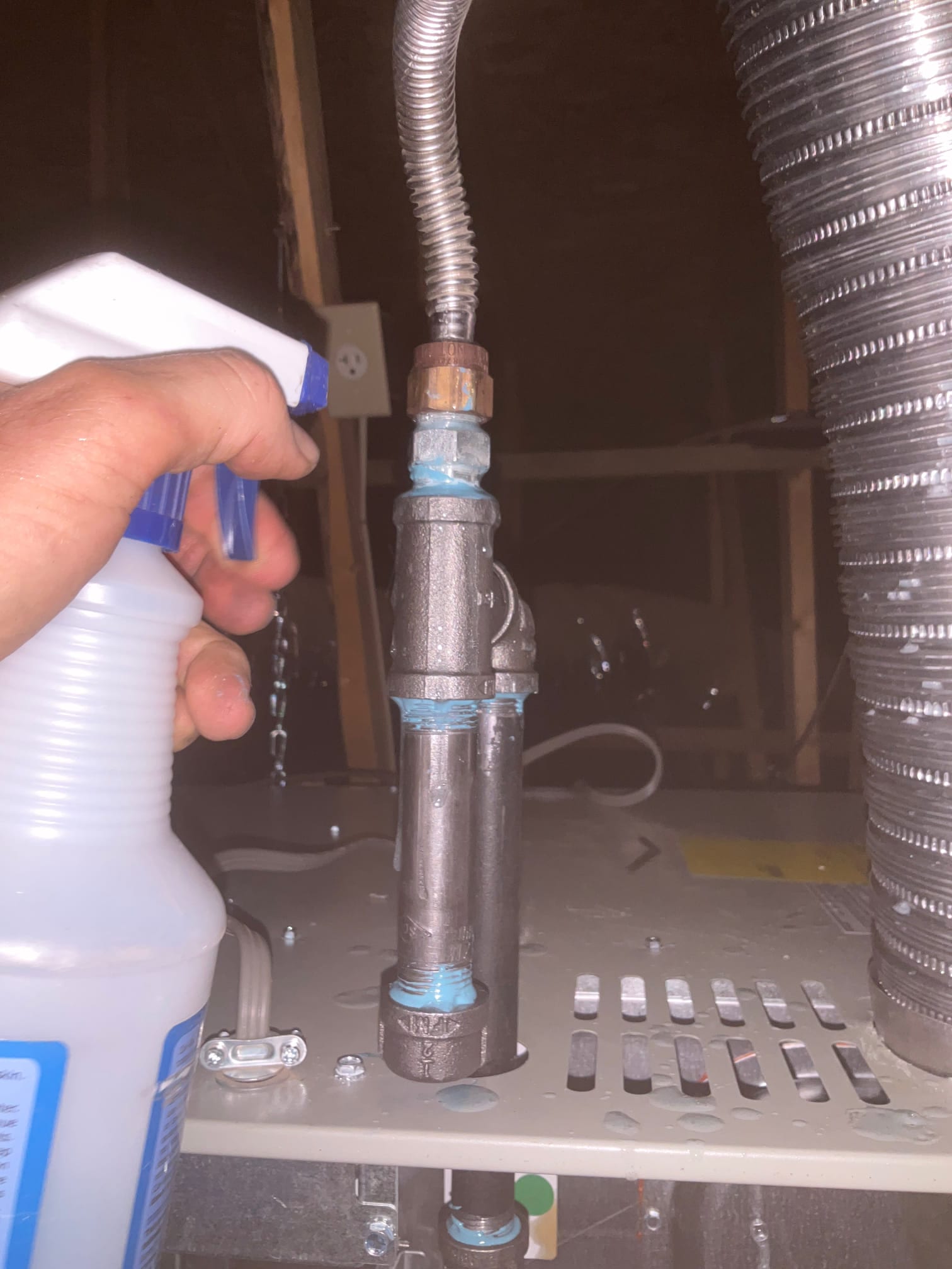 Technician sprays leak solution on newly assembled gas flex connector, drip leg, and union at the furnace during installation.