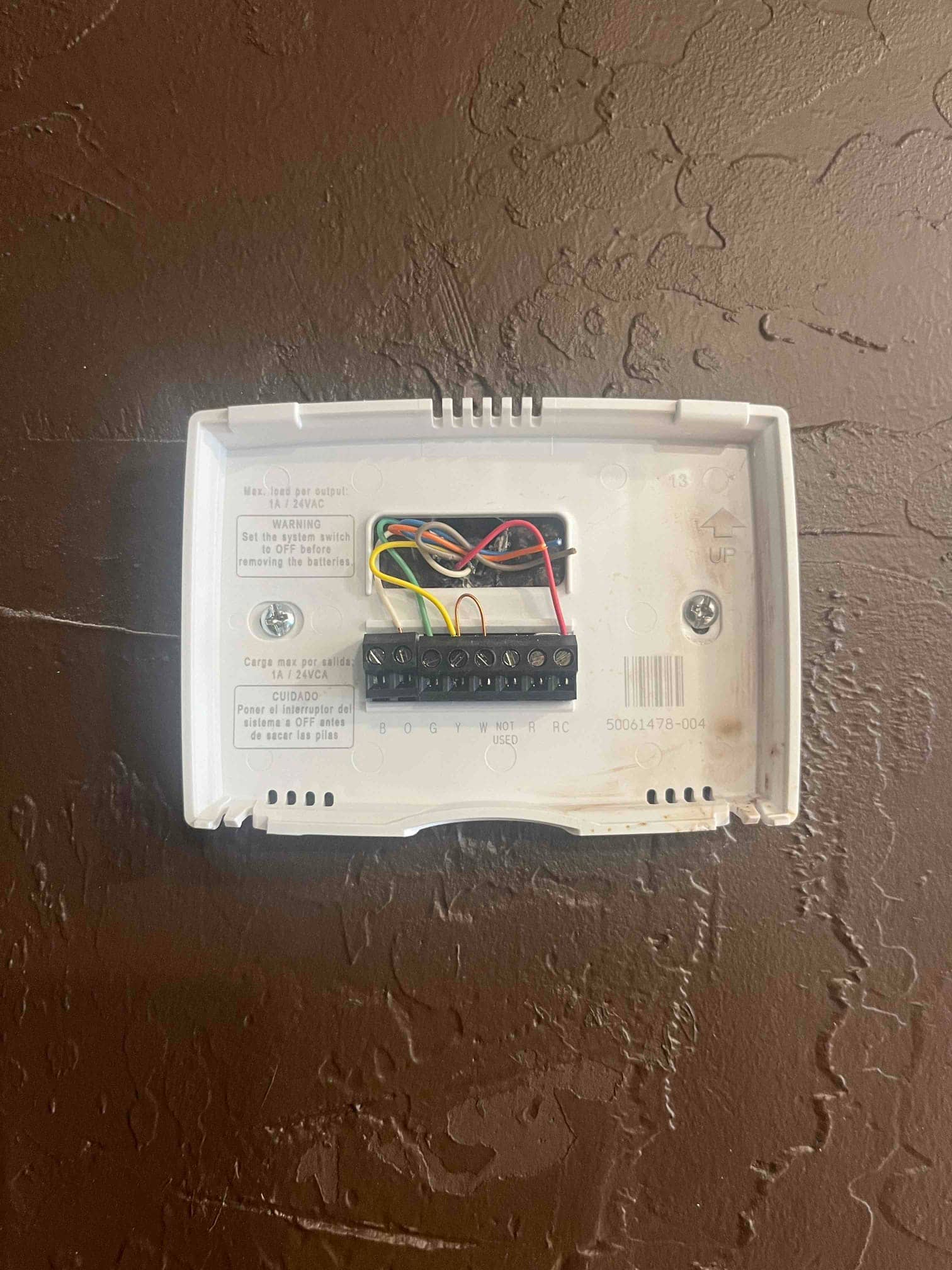 Thermostat wall plate with exposed control wiring to R, Y, G, W, and C terminals, cover removed during air conditioning repair.
