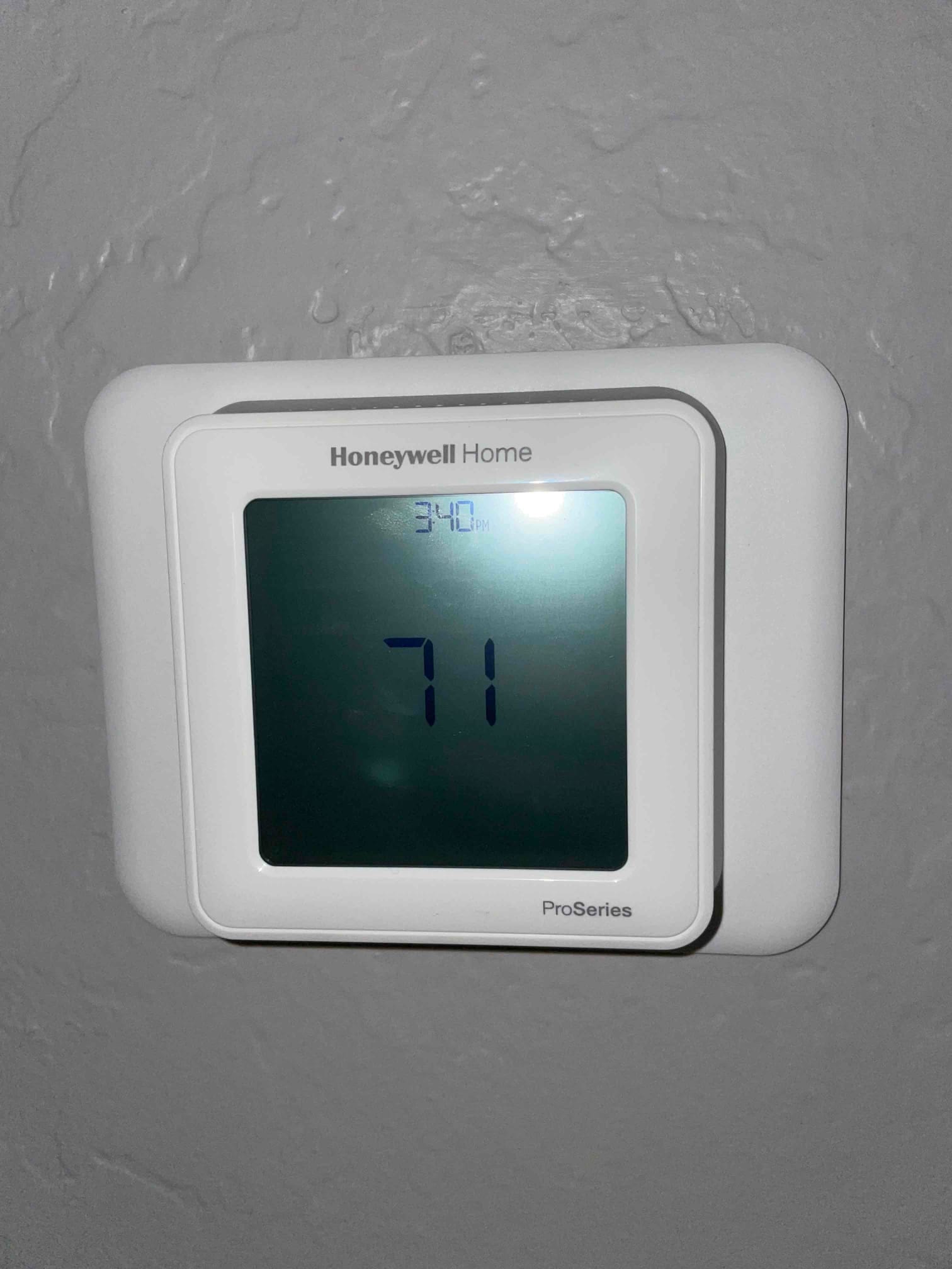 Wall-mounted digital thermostat displays 71 degrees after installation, confirming control interface for the new HVAC system.