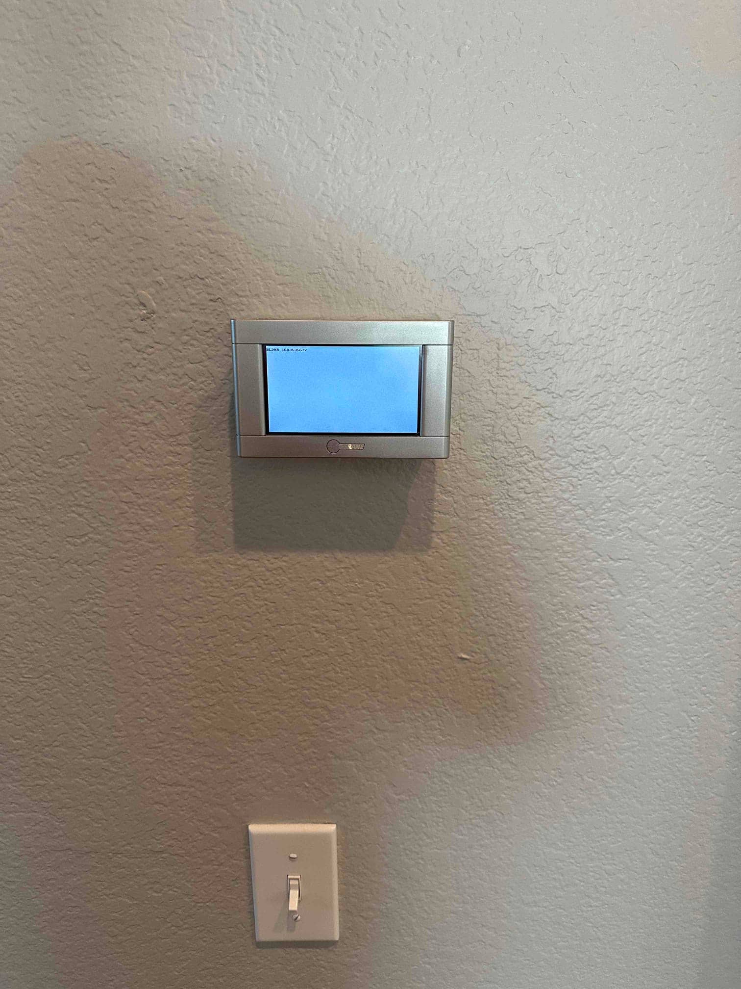 Wall-mounted digital thermostat installed and powered, shown above a light switch on a textured interior wall.