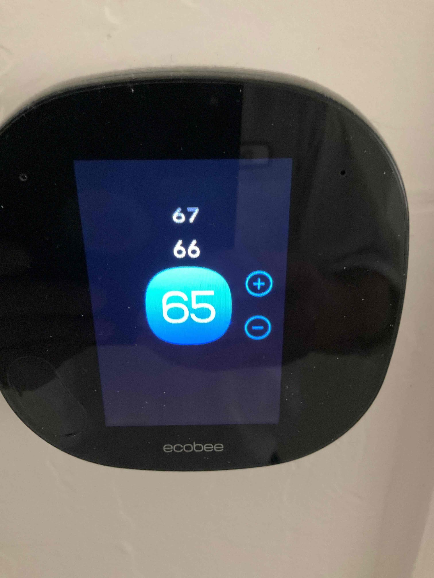 Wall-mounted smart thermostat display shows 65 set point with plus and minus controls and additional numbers 67 and 66.