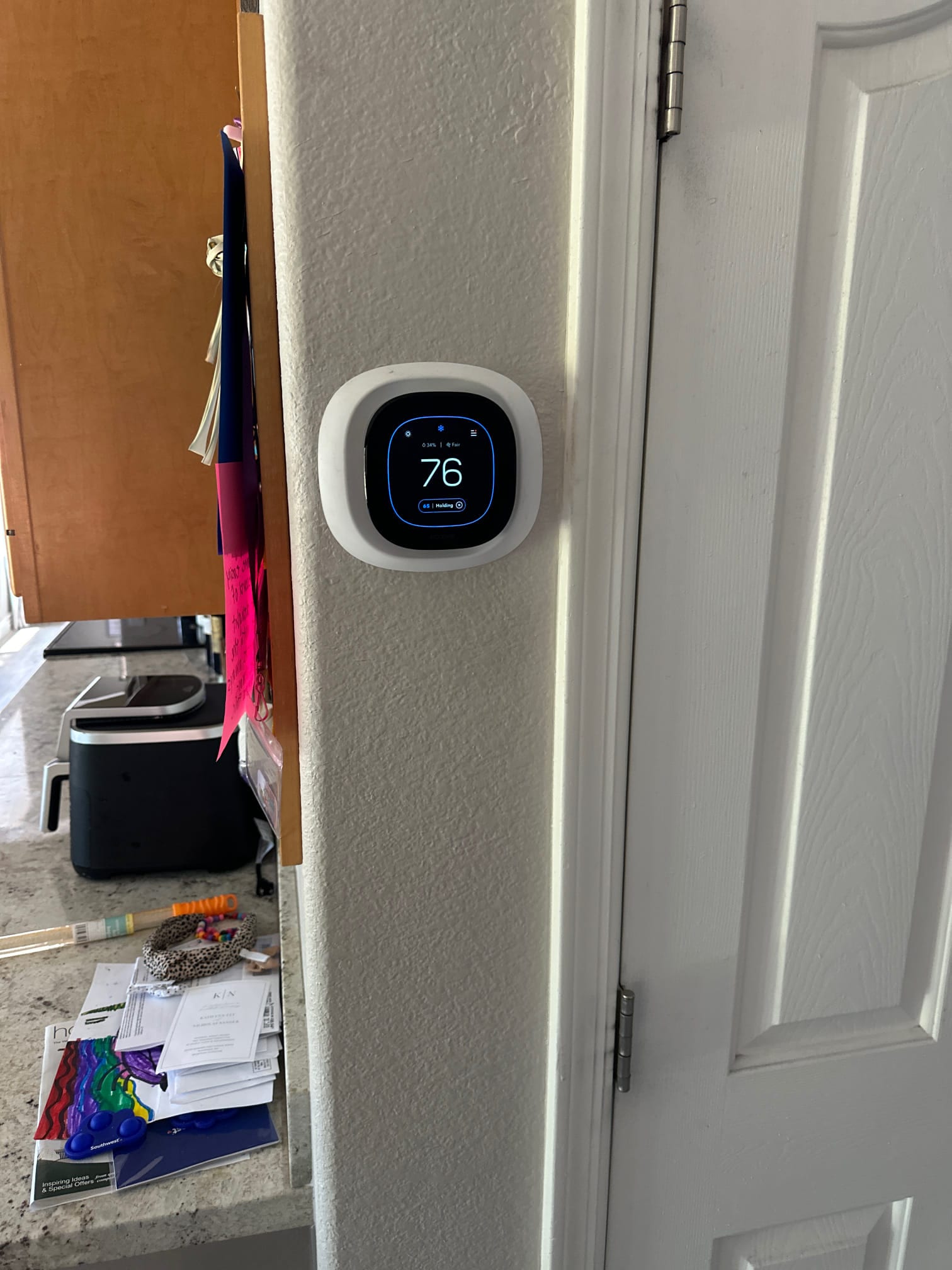 Wall-mounted smart thermostat installed and powered on, displaying indoor temperature and system status in a finished living space.